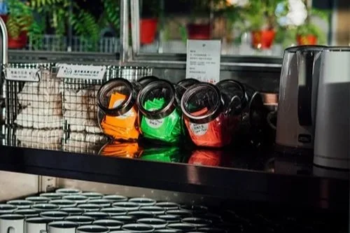 Jars of tea on a black shelf in a store.
