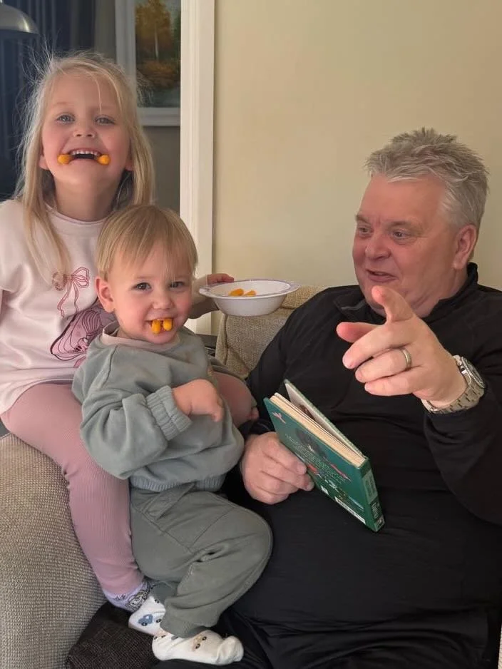 Paul reading a storybook with his two young grandchildren on the sofa