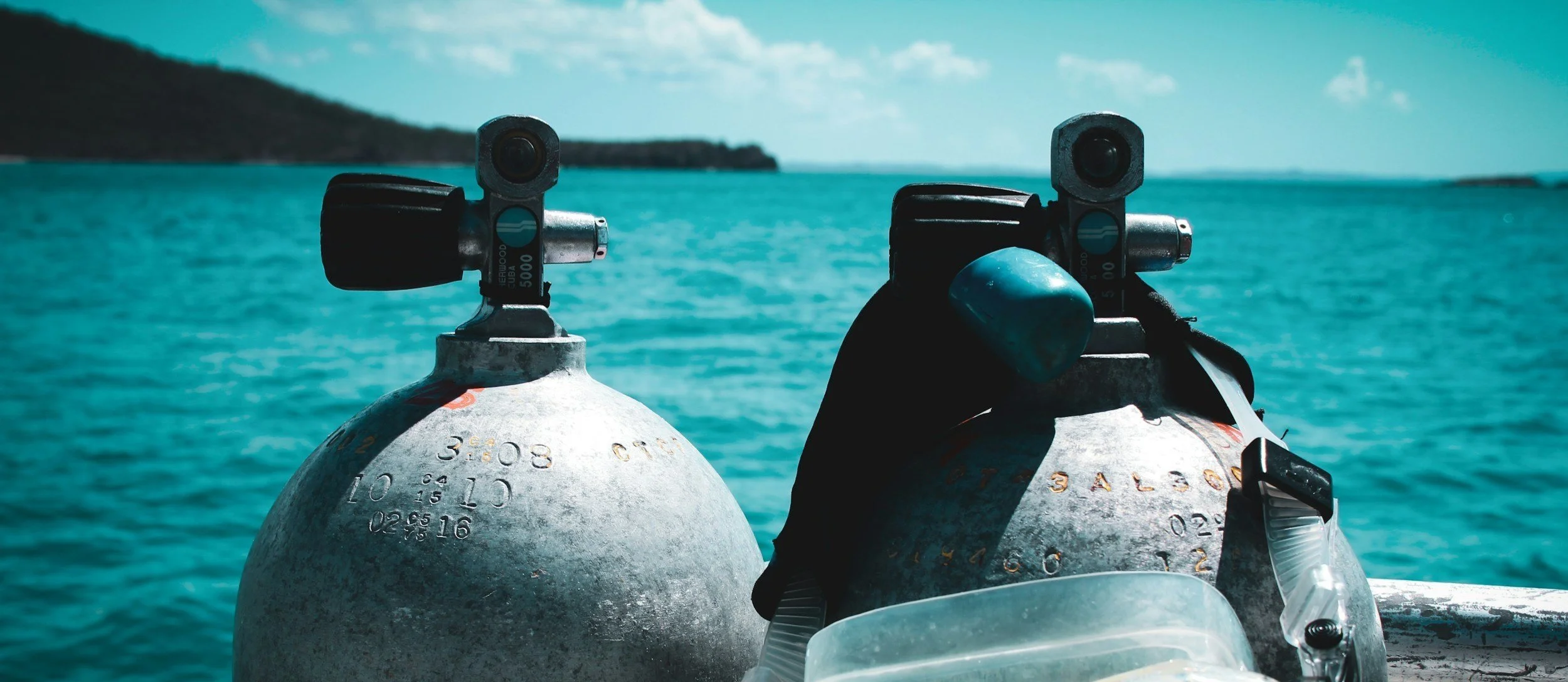 Two scuba diving tanks on a boat with a body of water and a distant shoreline in the background.
