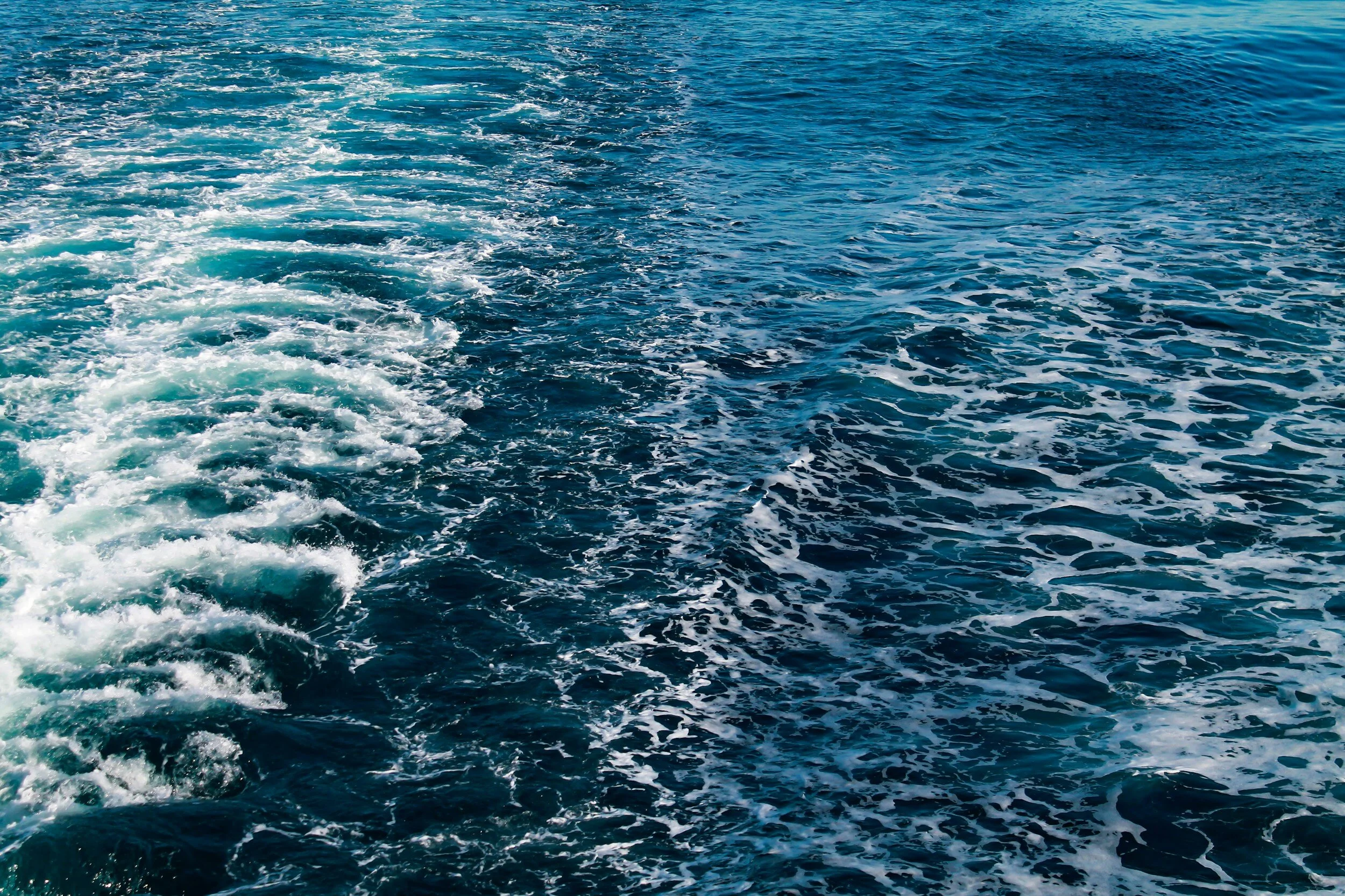 The image shows the ocean with a boat's wake, creating white foam and ripples in the water.