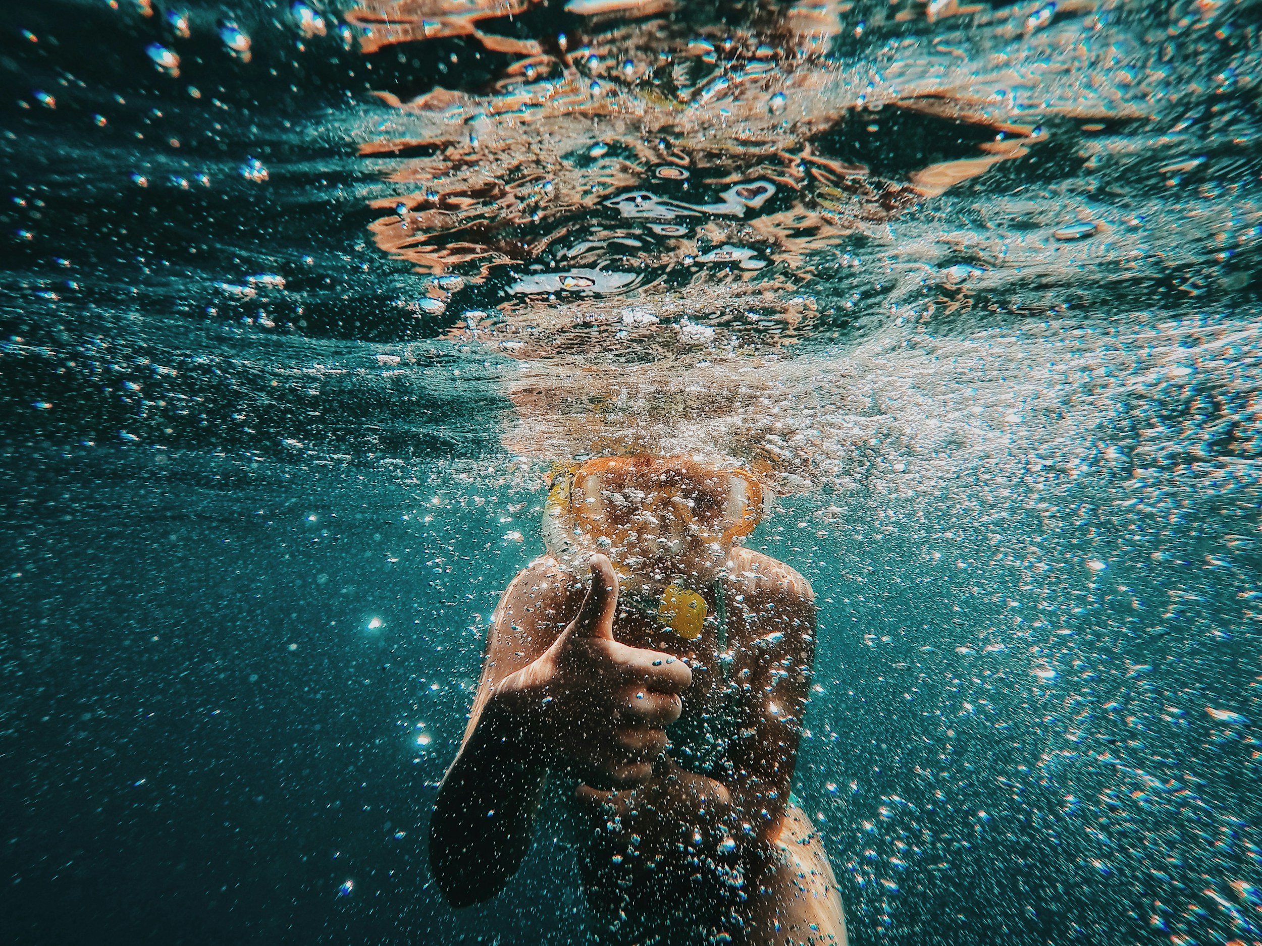 A person underwater giving a thumbs-up, surrounded by bubbles and water reflections.
