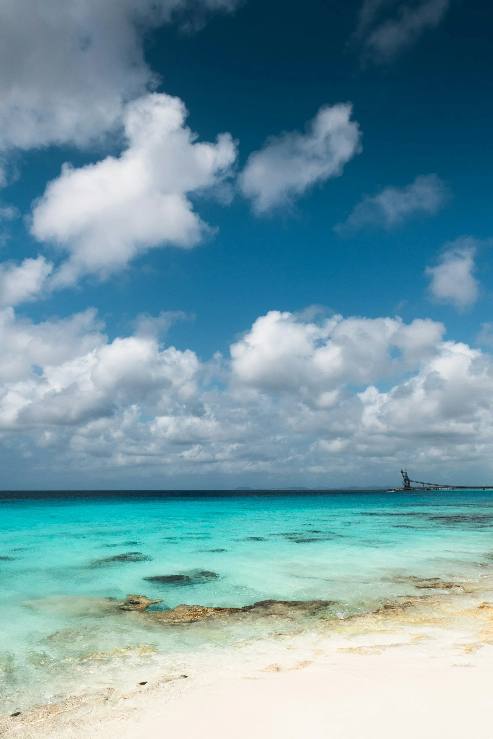 Tropical beach with clear turquoise water, white sandy shore, and a cloudy sky.