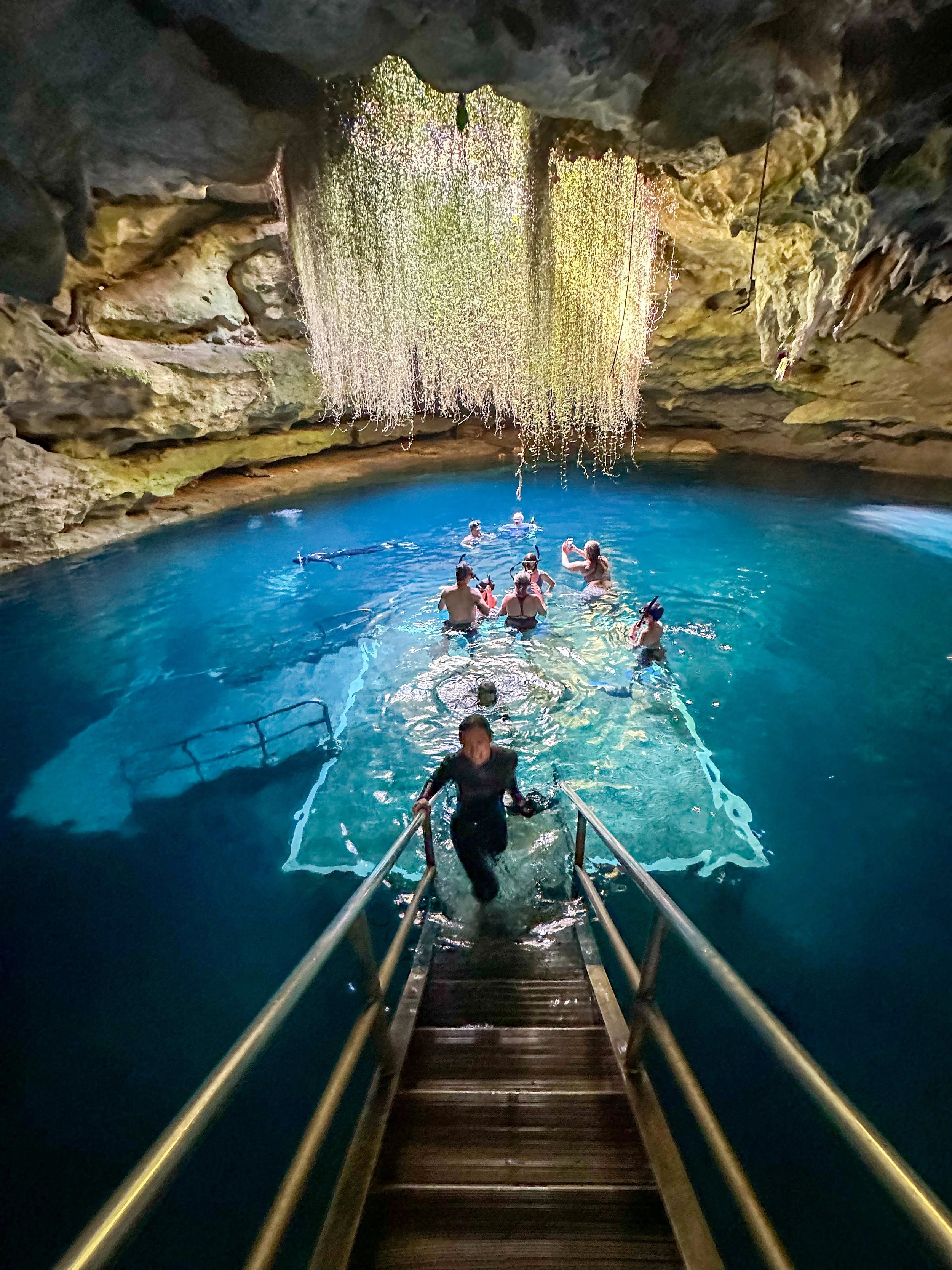 People swimming in a large underground cenote with a waterfall at the top and rocky walls surrounding the water