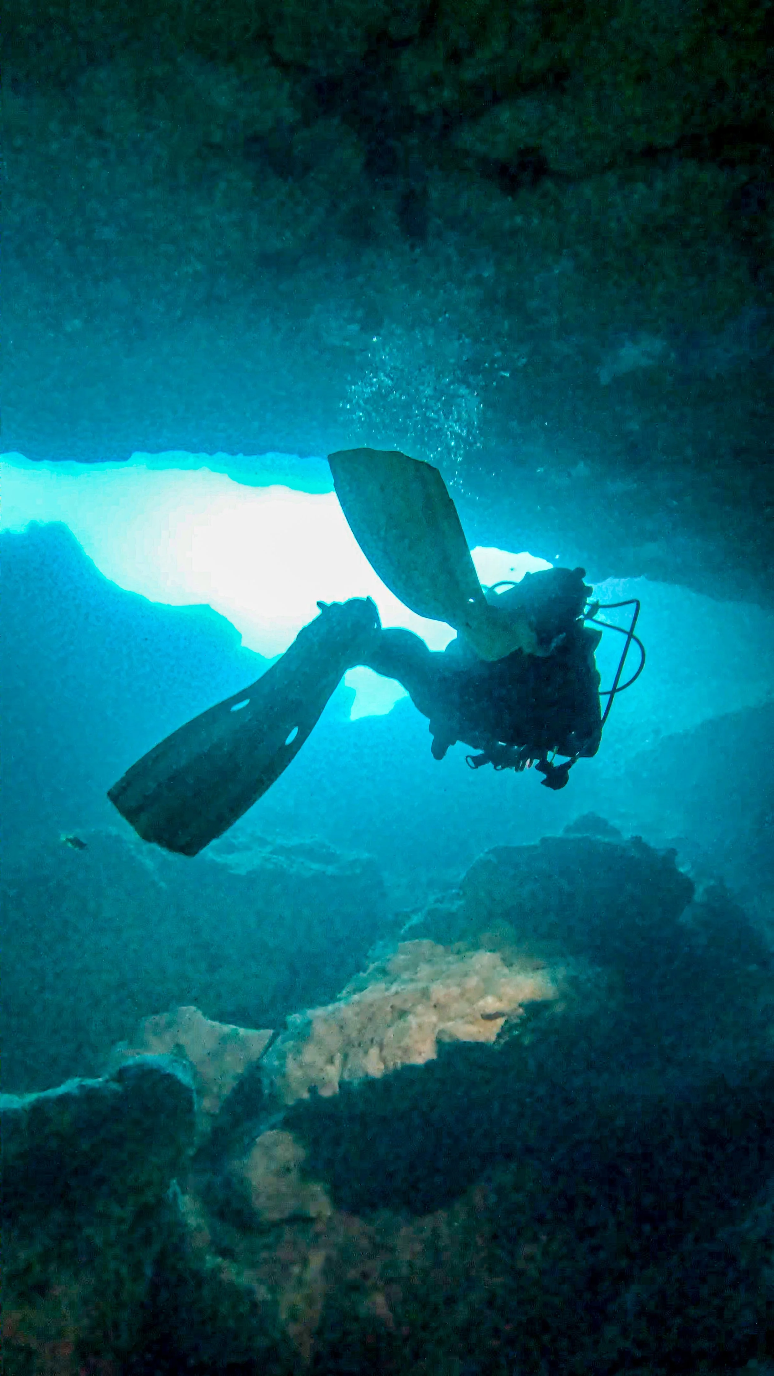 Silhouette of a scuba diver swimming in an underwater cave or cavern with sunlight shining from above.