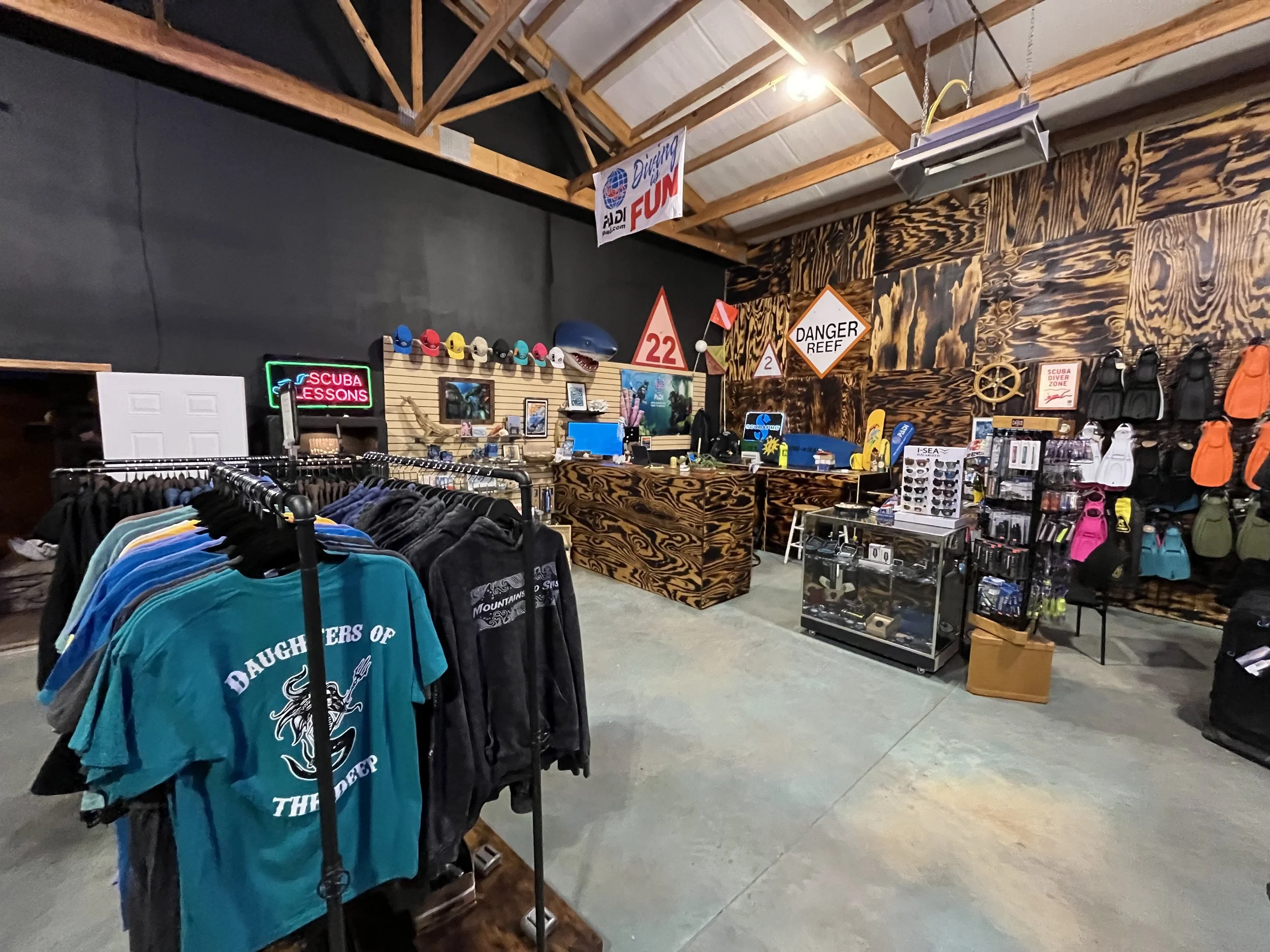 Interior of a store with scuba diving gear, clothing, and accessories on display, including hats, backpacks, and signs related to diving and safety.