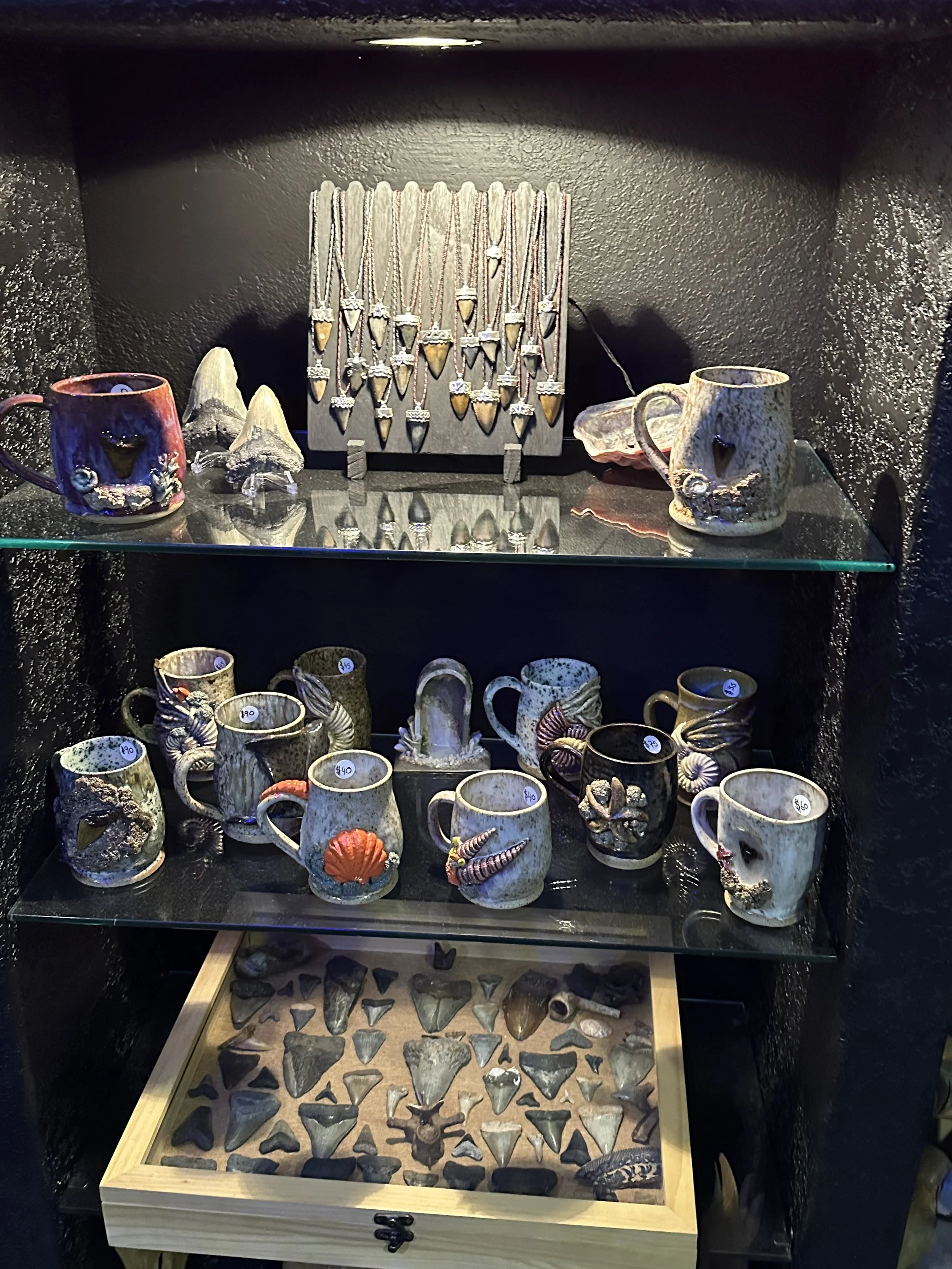 A display of handmade ceramic mugs, necklaces, and arrowhead-shaped artifacts in a black shelving unit.