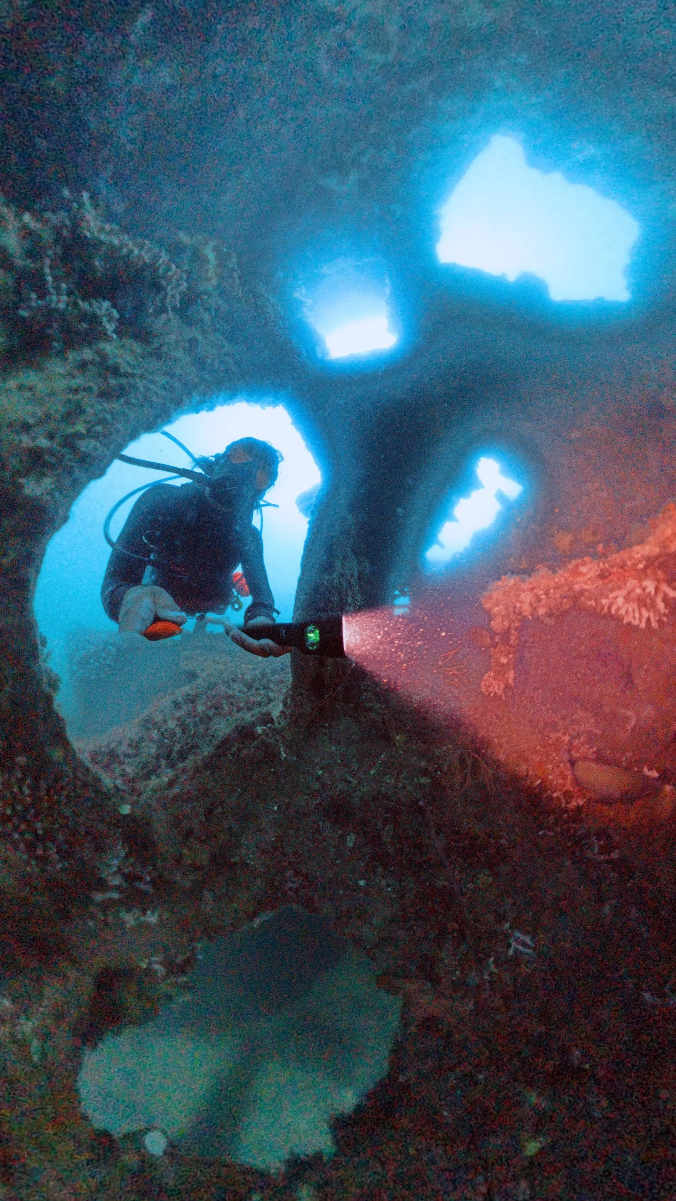 A scuba diver exploring an underwater cave with openings in the rock, illuminated by diver's flashlight.
