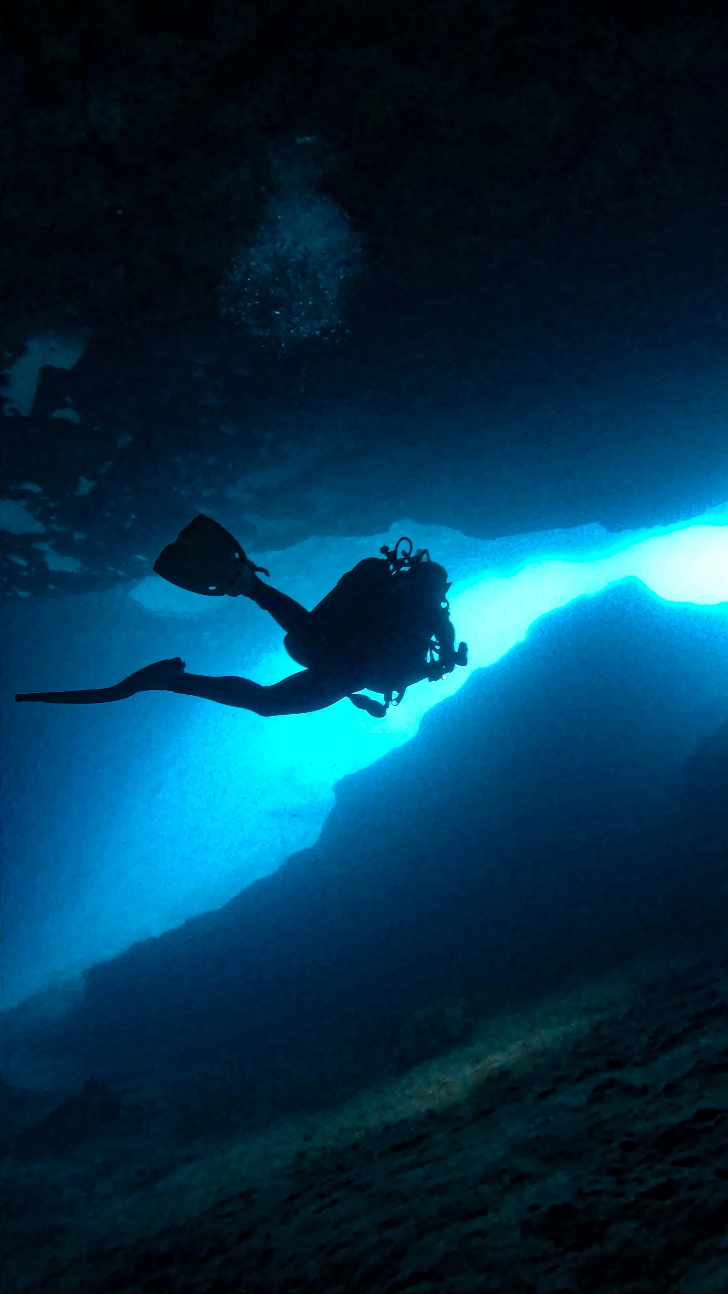 Silhouette of a scuba diver exploring an underwater cave with light filtering through the entrance.