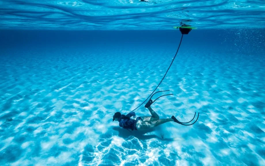 Person scuba diving underwater with a tethered underwater drone above.