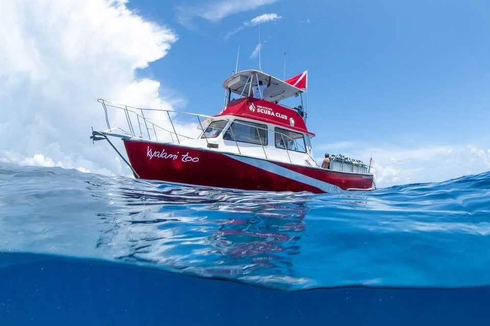 A red and white boat named Kyalami Too on clear blue water with a partly cloudy sky in the background.