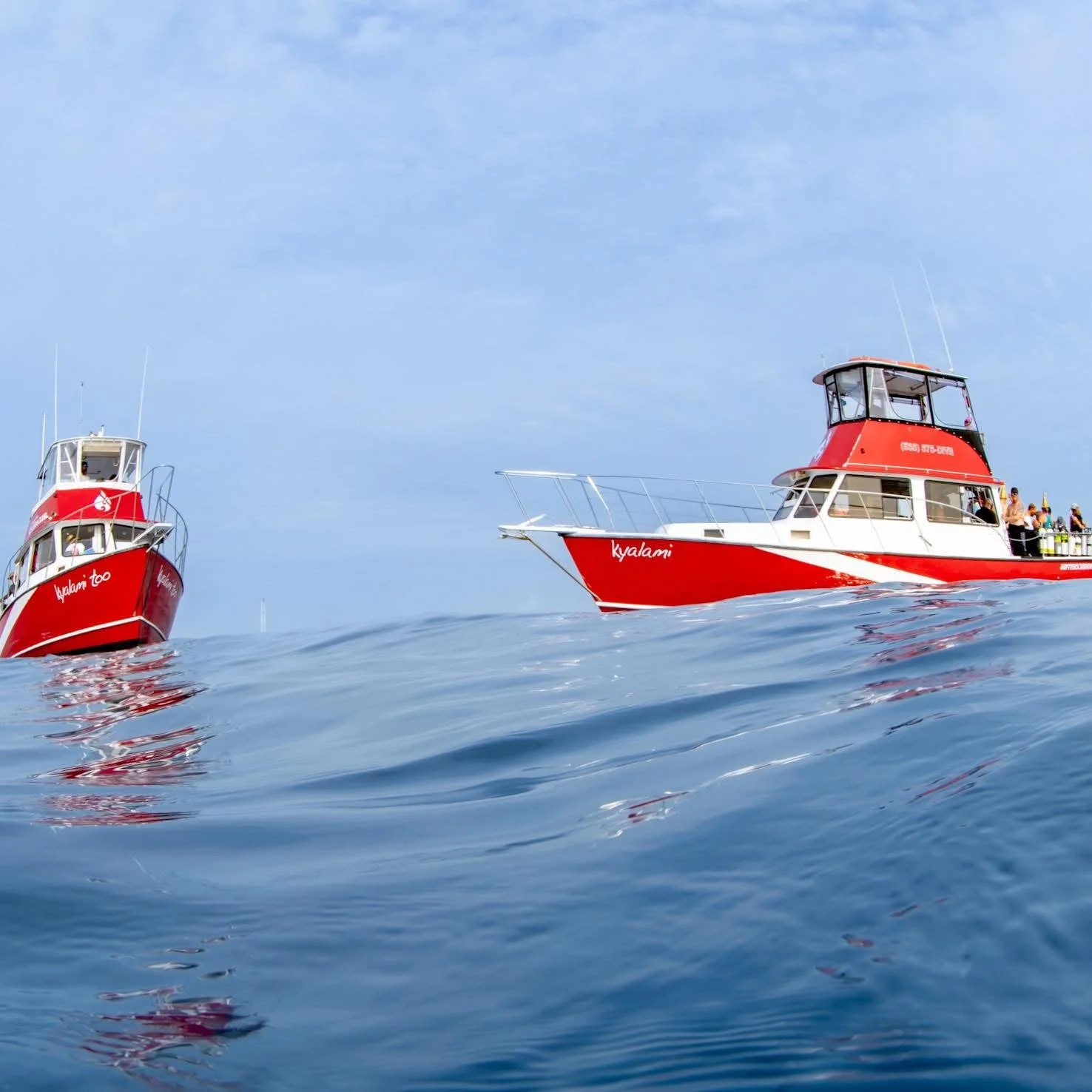 Two red and white boats on calm ocean water with a cloudy sky.