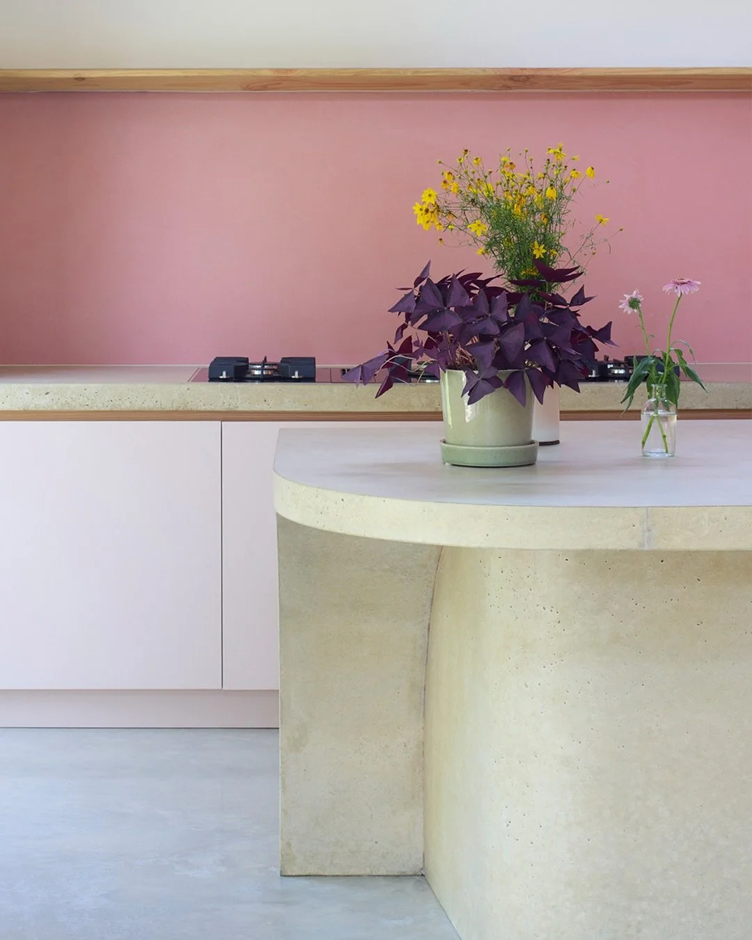 UP AND OVER

The kitchen island is a solid, sculptural form which flows from the dining space into the kitchen, creating a cantilevered surface which becomes a sociable space for seating. The kitchen splashback is formed in pink concrete. The kitchen