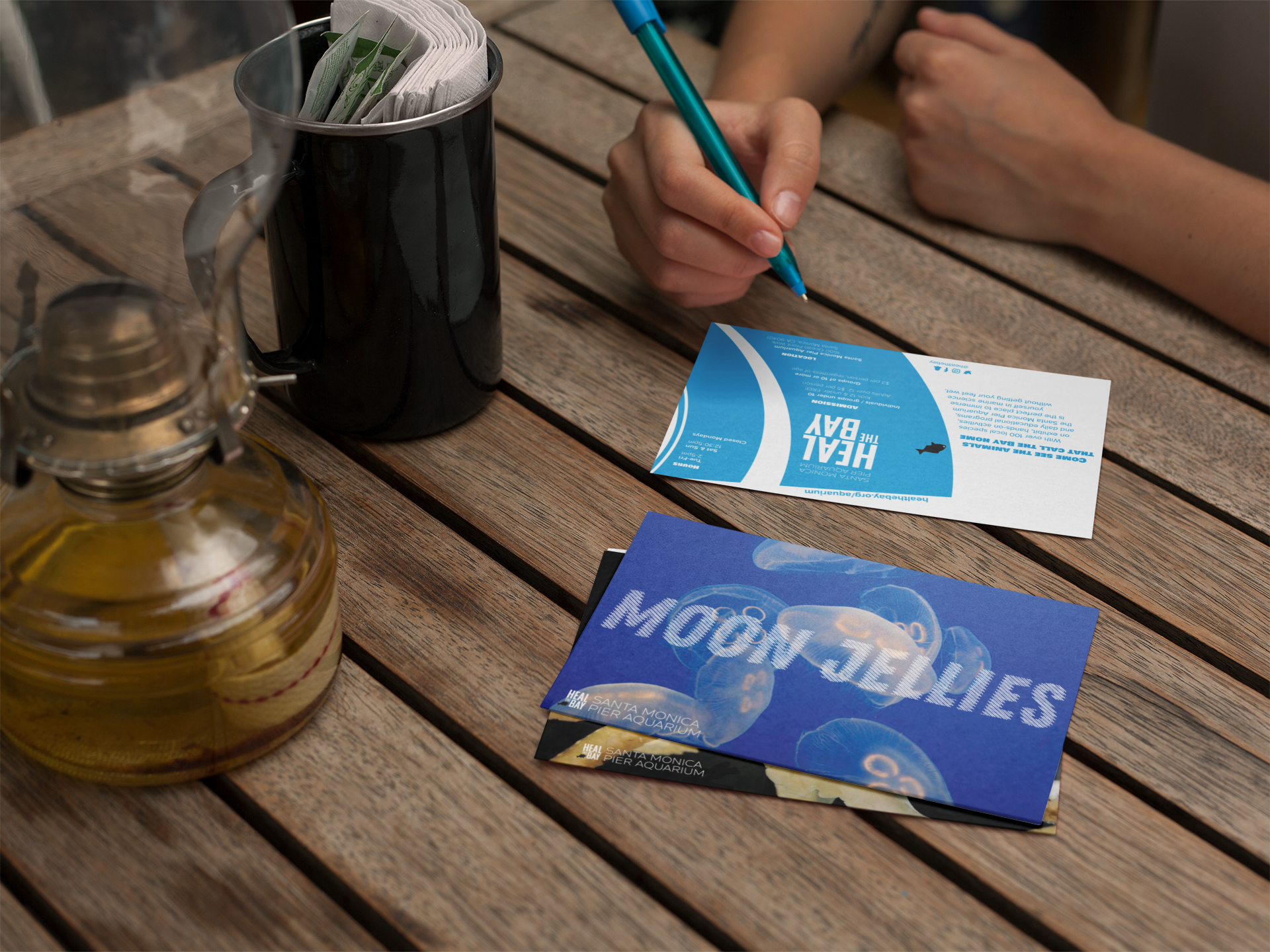 girl-about-to-write-on-a-postcard-mockup-while-other-postcards-lying-on-a-wooden-table-a14746.png