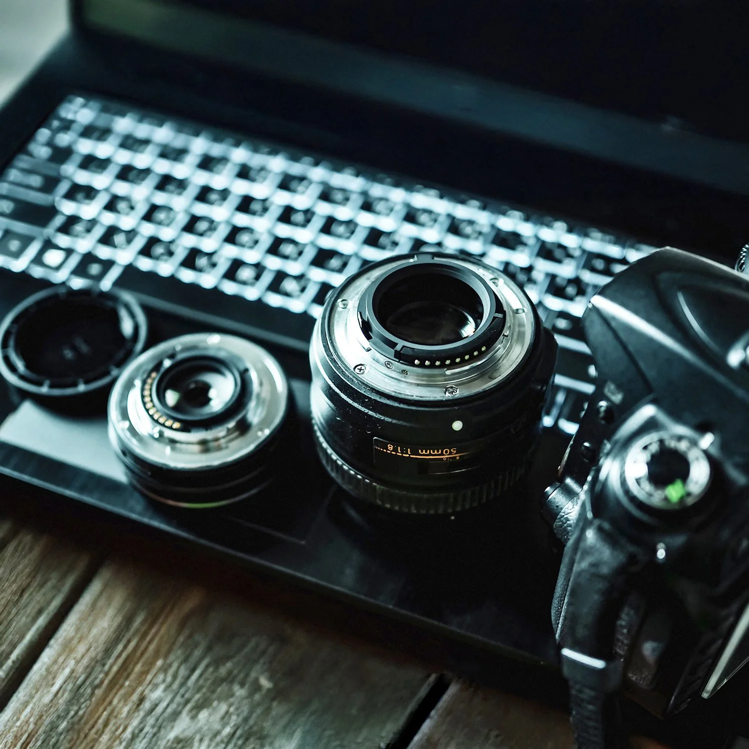 A digital camera, camera lenses, and camera accessories on a laptop keyboard.
