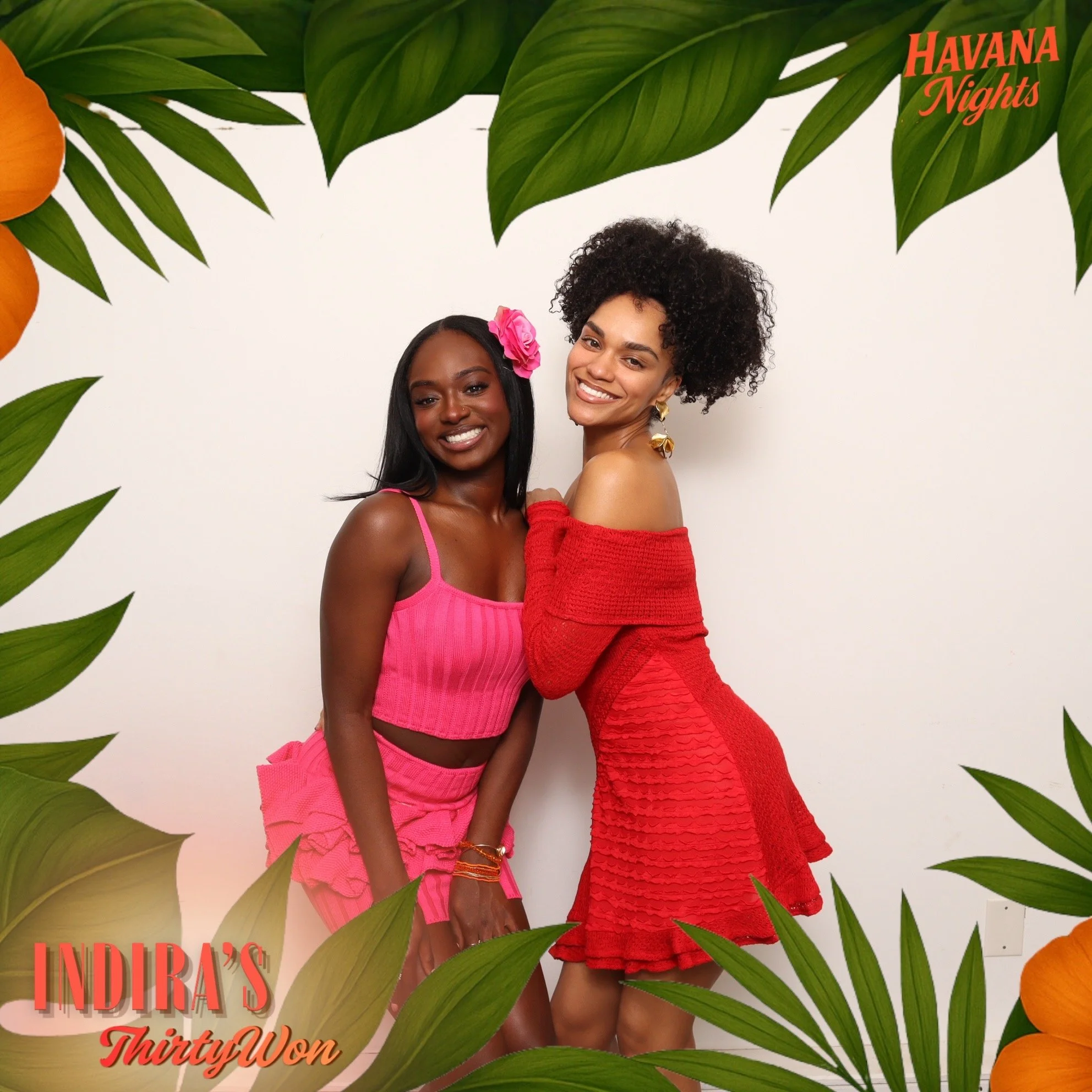 Two women in pink and red dresses standing together, smiling against a plain white background, surrounded by a border of green tropical leaves and orange flowers, with text "Havana Nights" in the top right corner and "Indira's ThirtiyWon" in the bottom left corner.