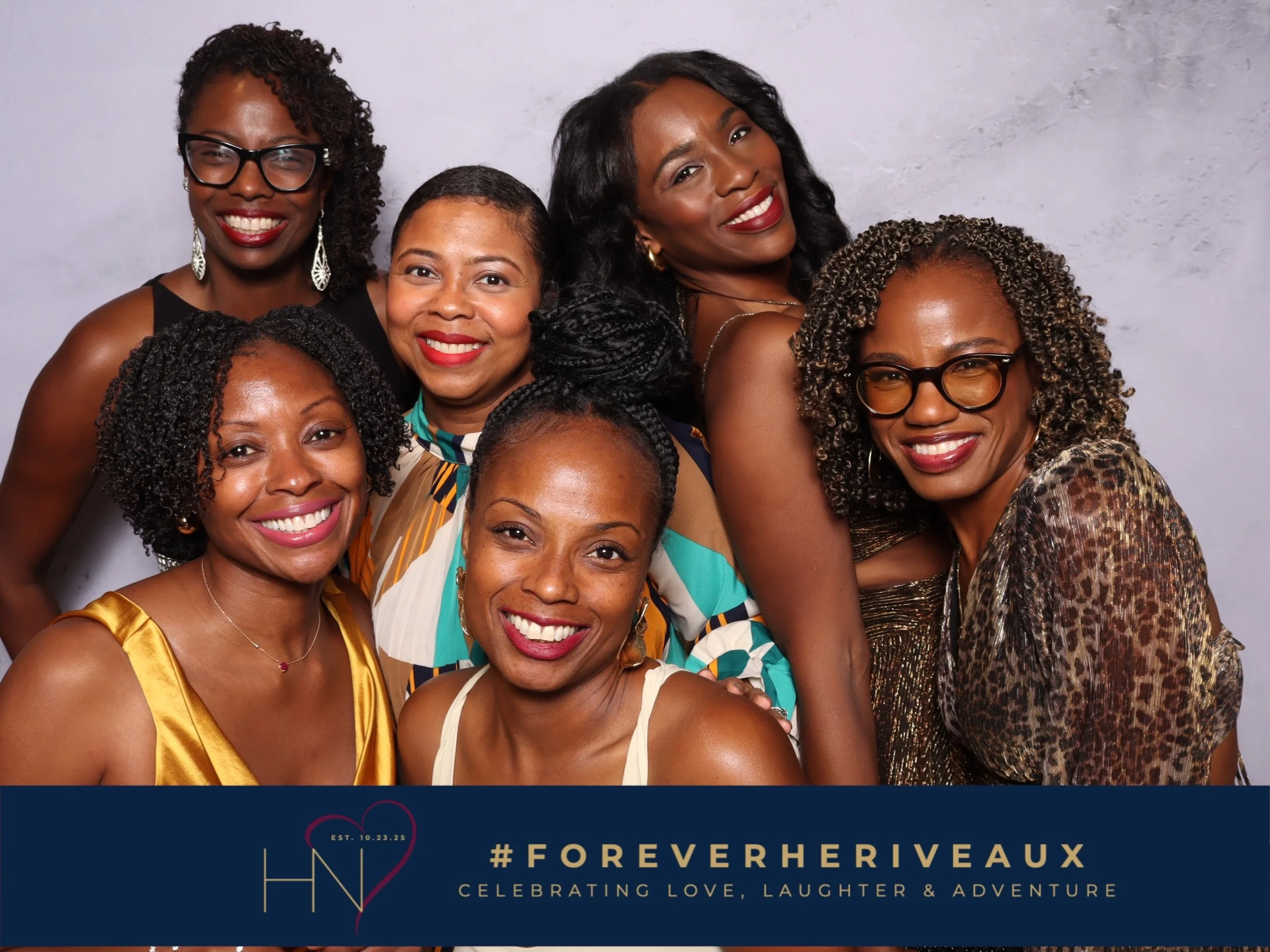 Group of seven women smiling and posing for a photo against a neutral background, with a banner at the bottom reading 'Forever Hervéaux' and '#ForeverHerveaux', celebrating love, laughter, and adventure.