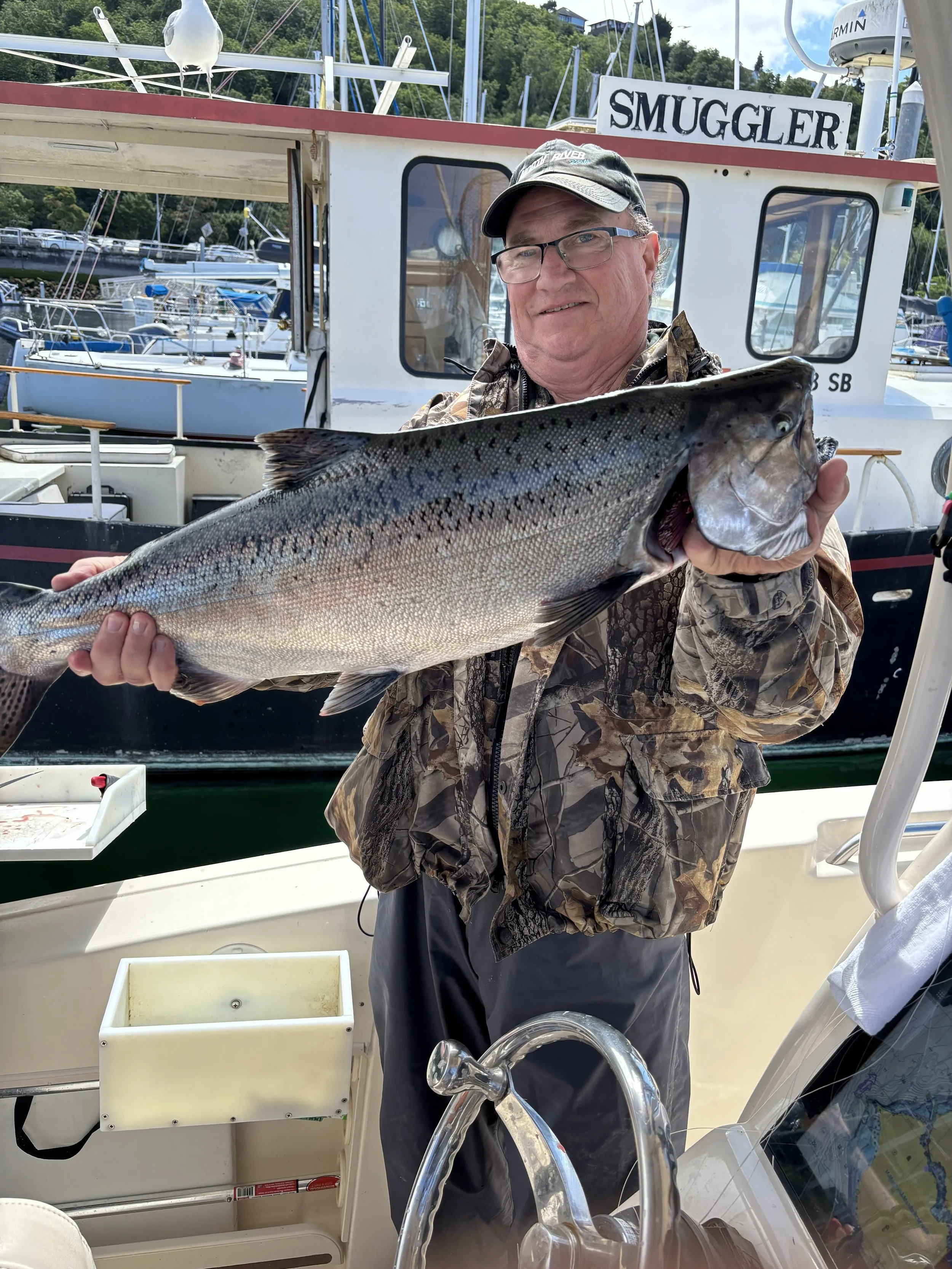 A man dressed in camo displaying a hatchery chinook salmon caught in area 10 puget sound july 2026 on board www.salmonseattle.com fishing charters