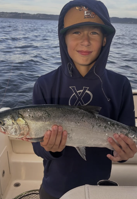 Young boy on a boat holding a large fish, with water and sky in the background.