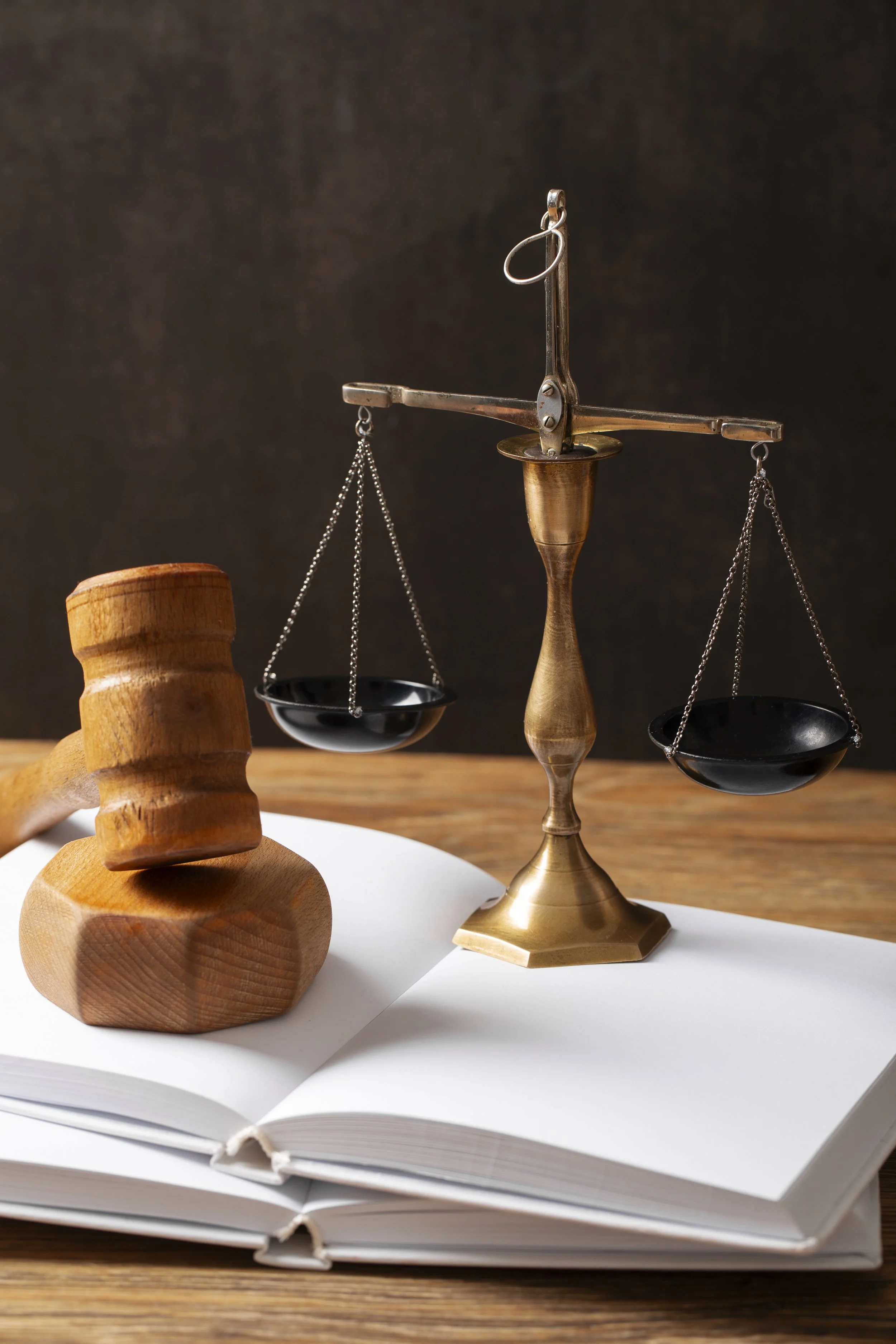 Une balance de justice en métal, un marteau en bois, et un livre ouvert sur une surface en bois.