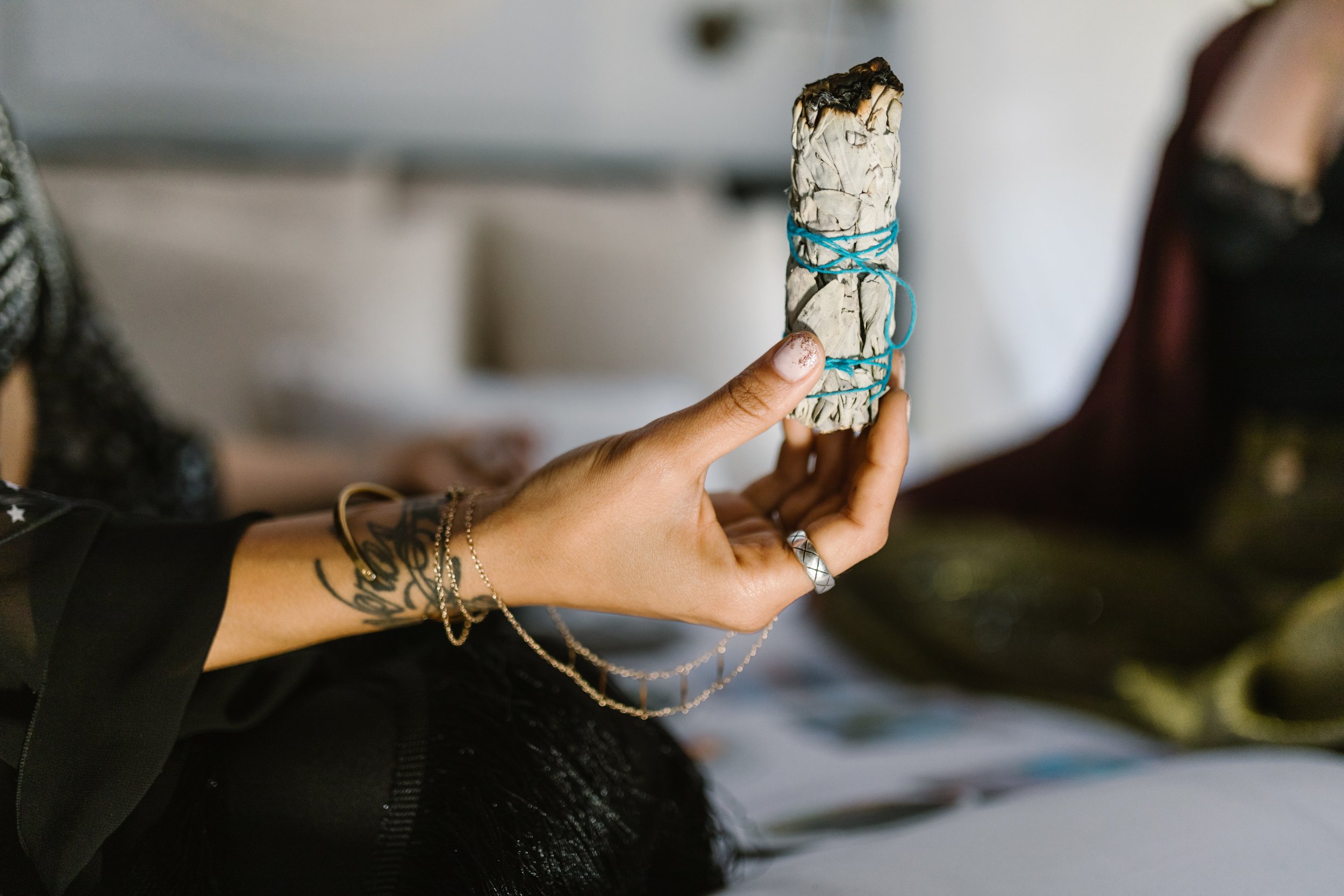 a woman is holding white sage wrapped in a blue ribbon. she is clearing the energy of the space before practicing mediumship development.