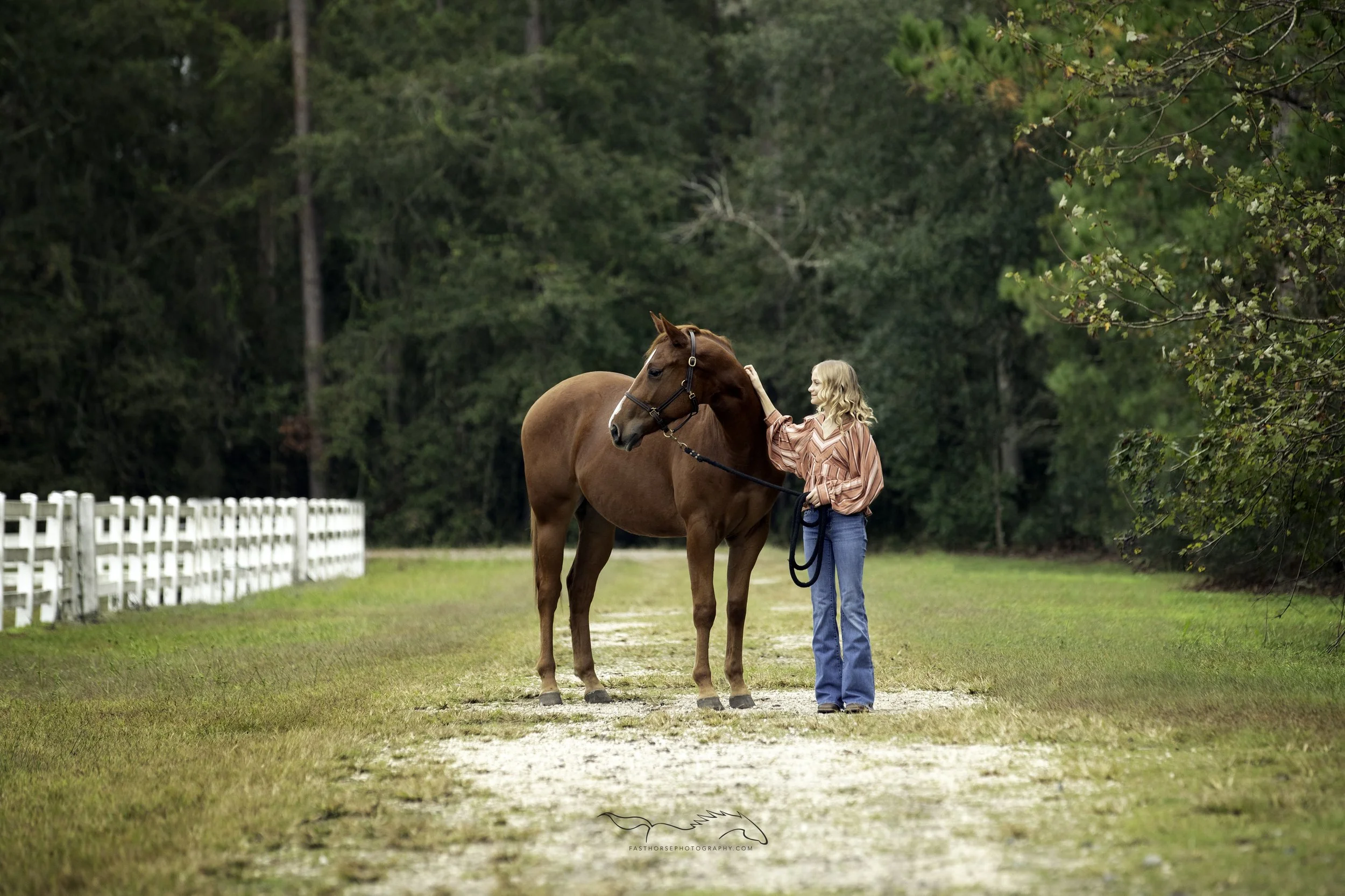 young girl stands with her horse looking over a fence