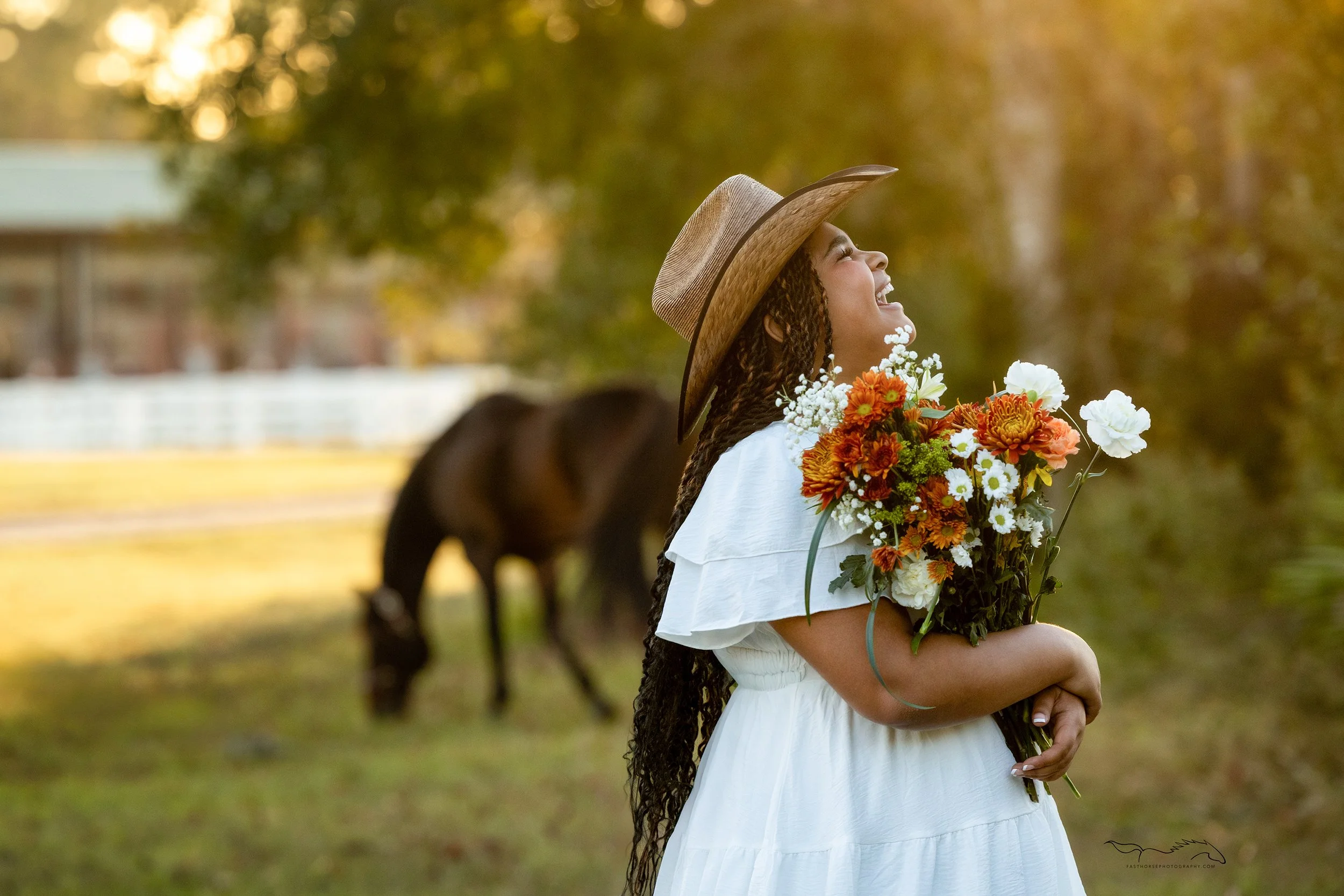 girl holding flowers and laughing while her horse grazes in the background