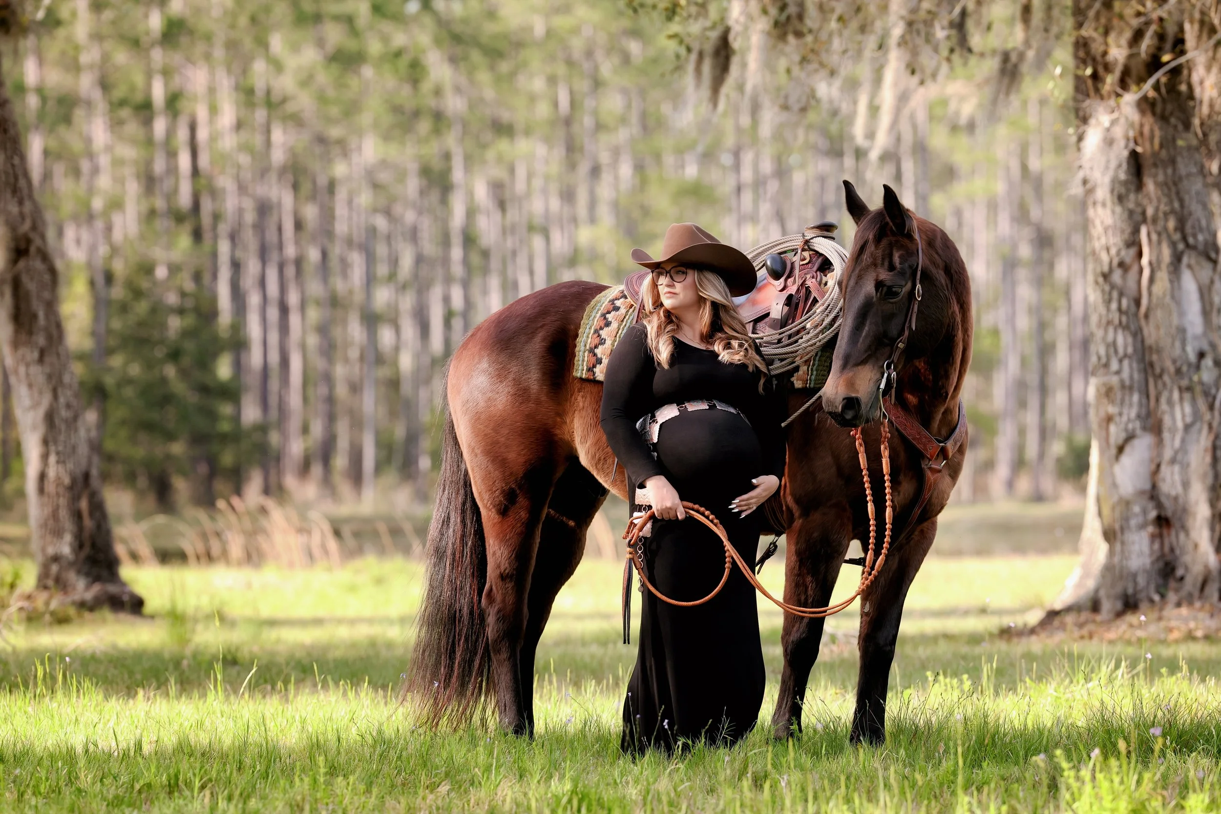 Woman stands with her horse under oak trees for a maternity photography session