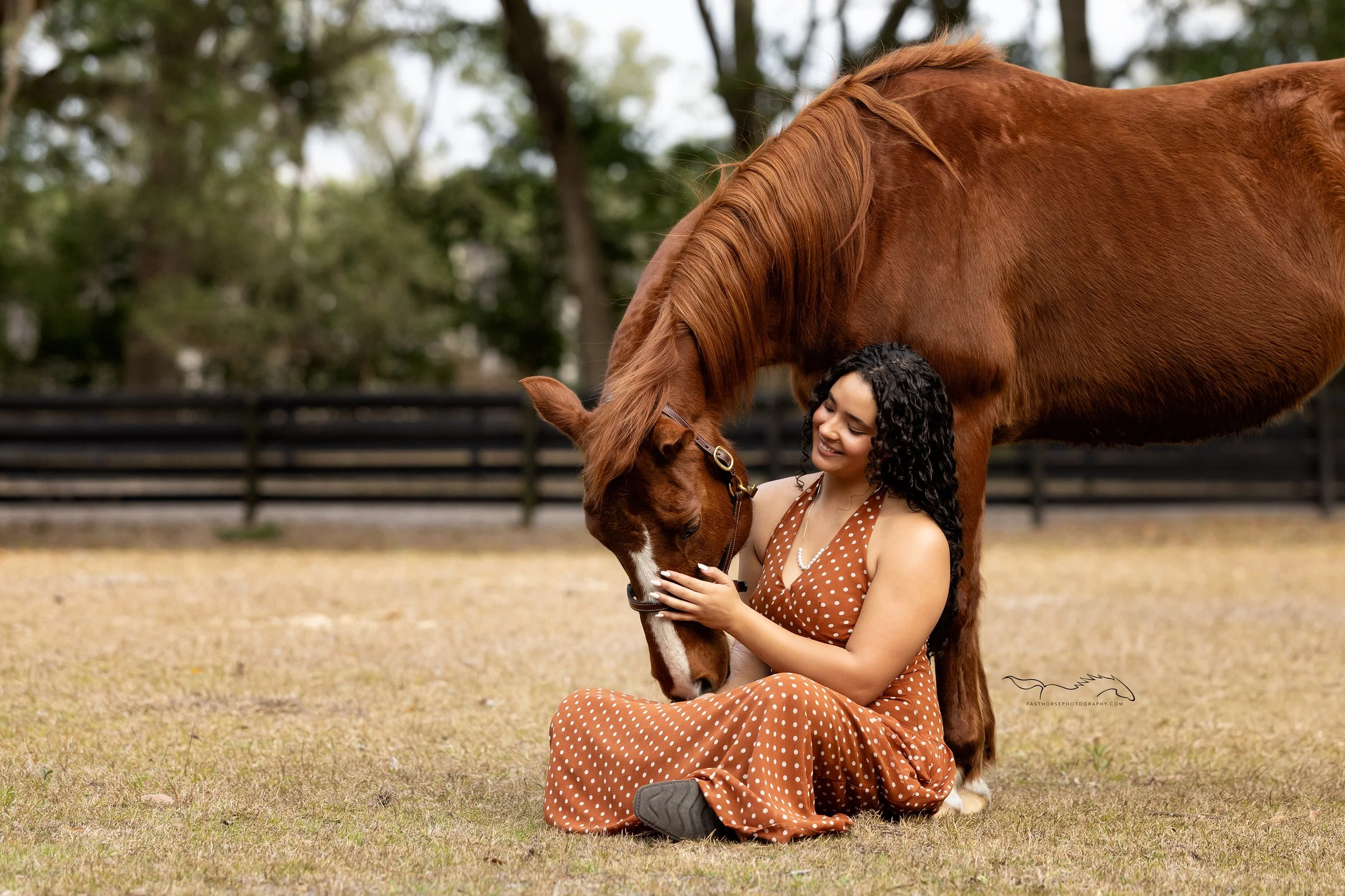 young woman sits on the ground cuddling with her horse