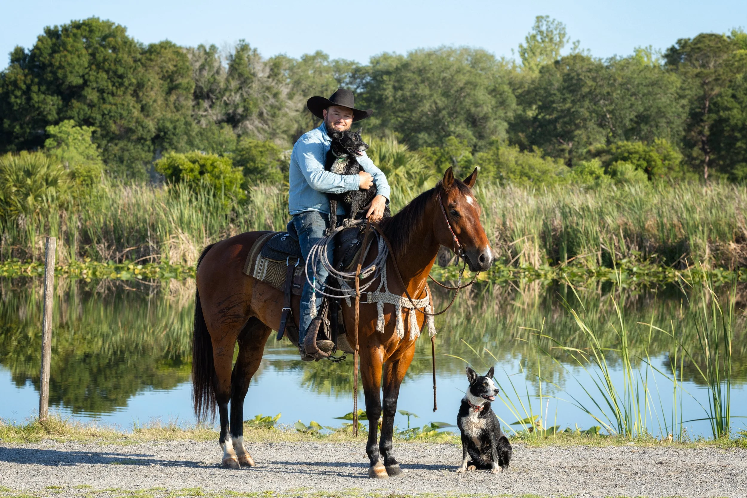 Jesse Mayher mounted on his horse with his two dogs by his side in front of a Florida wetland
