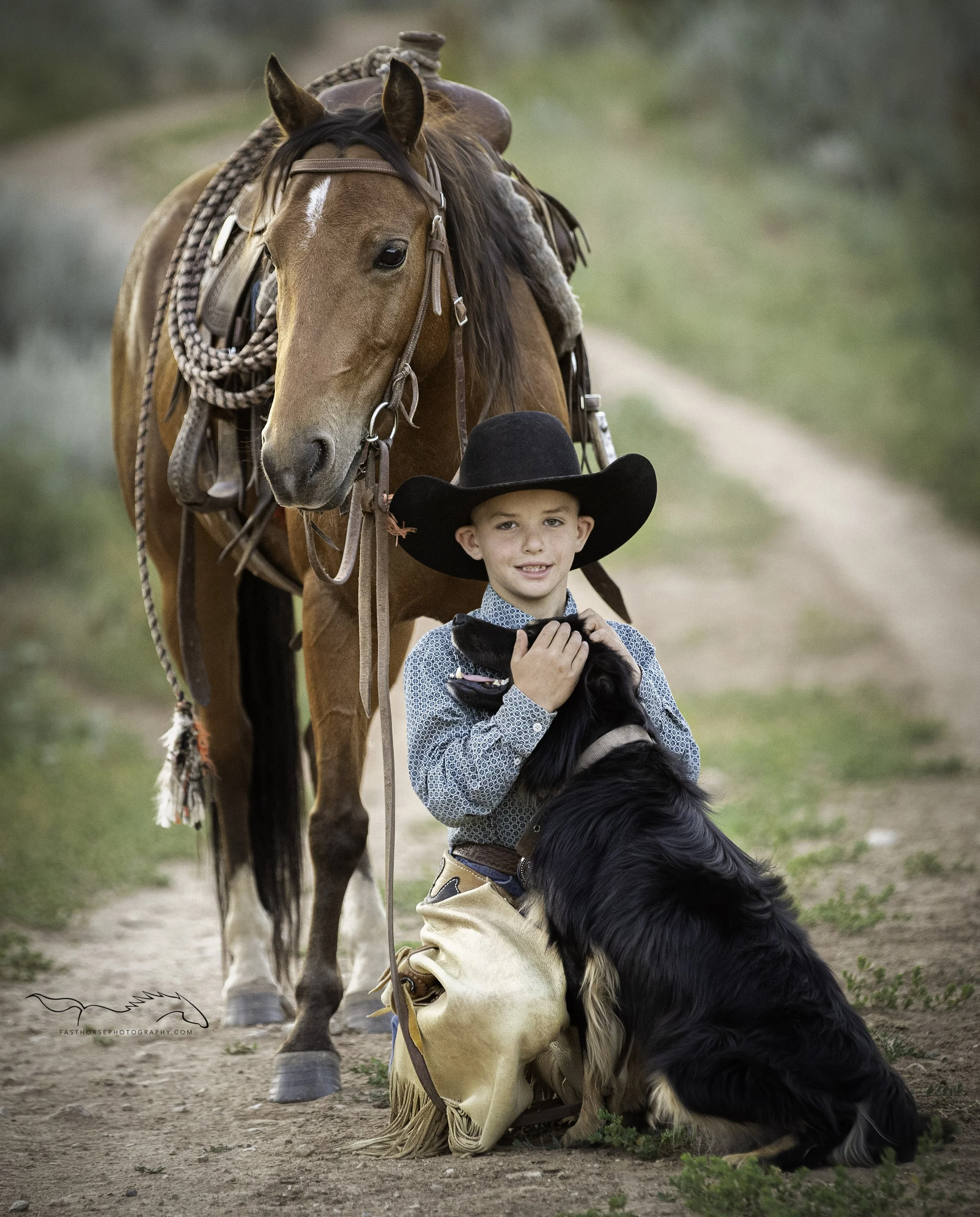 pre-teen boy kneels in front of his pony and pets his dog