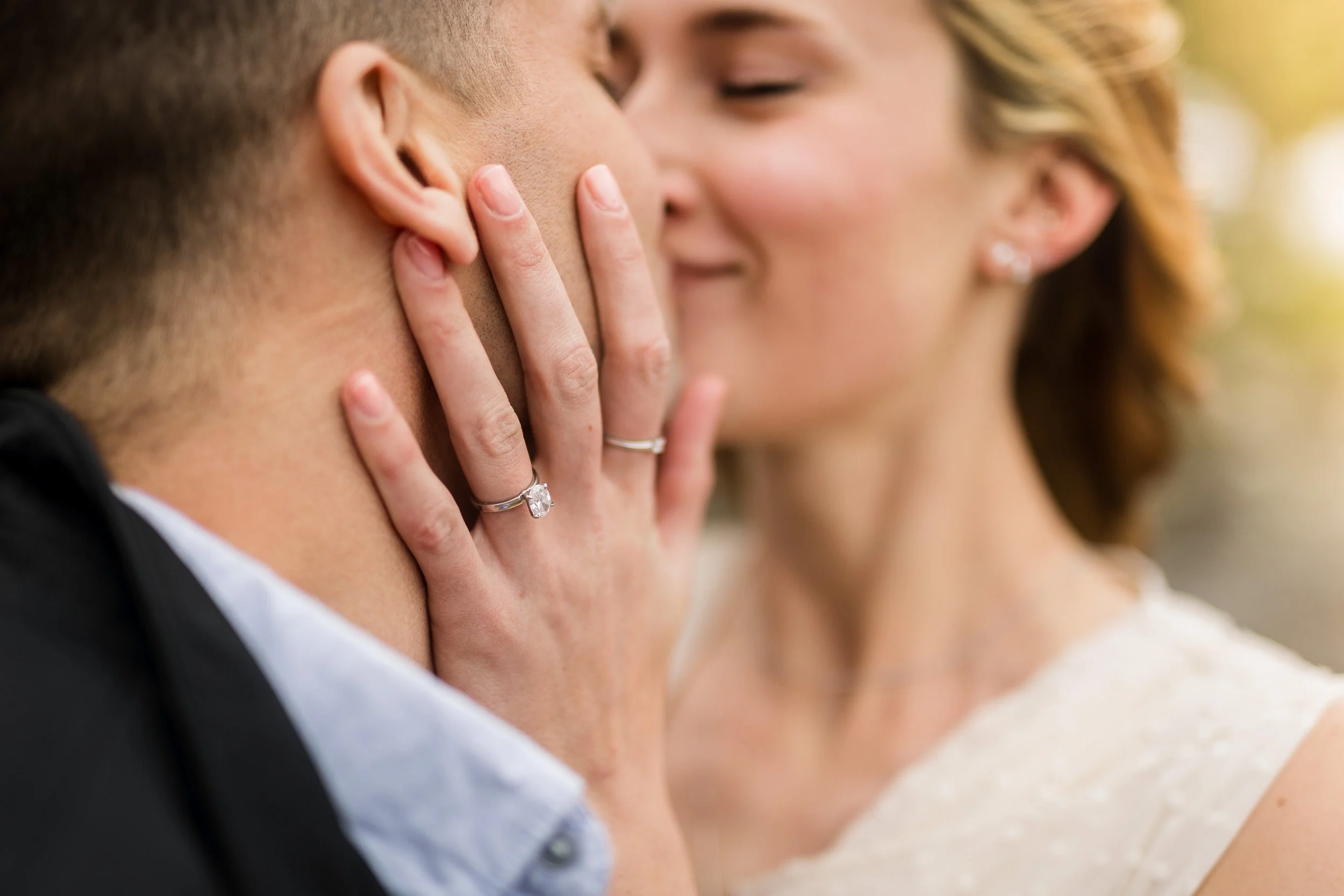 Engagement photo of couple kissing with ring in focus
