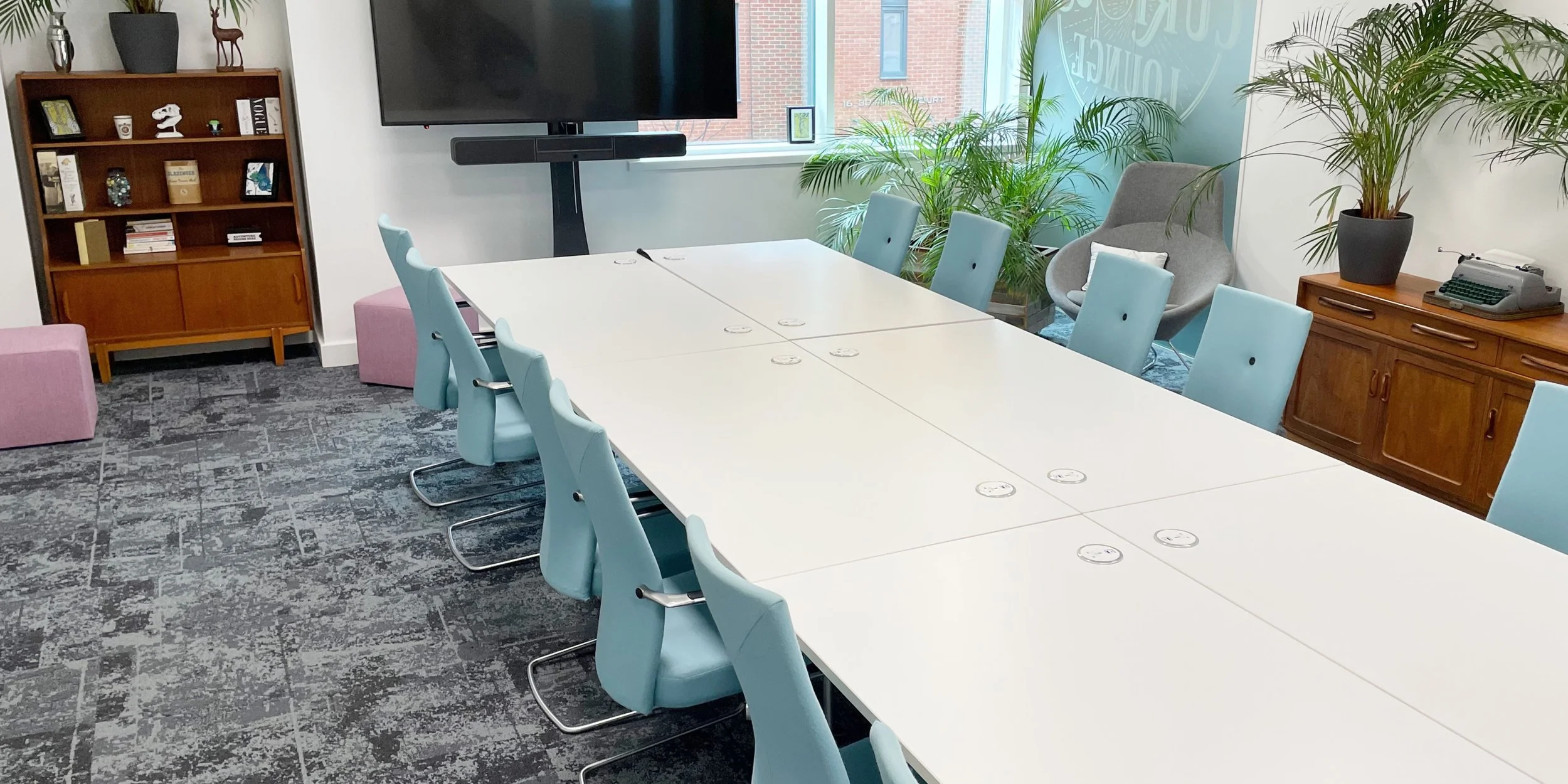 A boardroom with white tables, pale blue chairs and a giant screen
