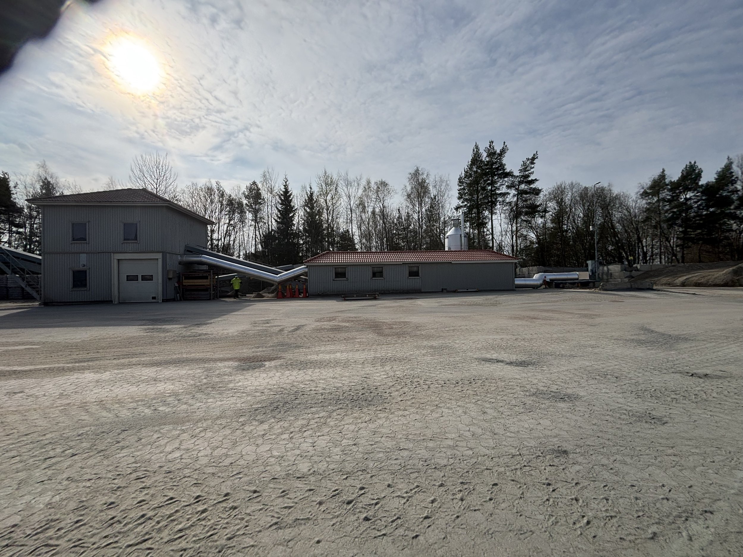 Industrial area with buildings, conveyors and surrounding trees.