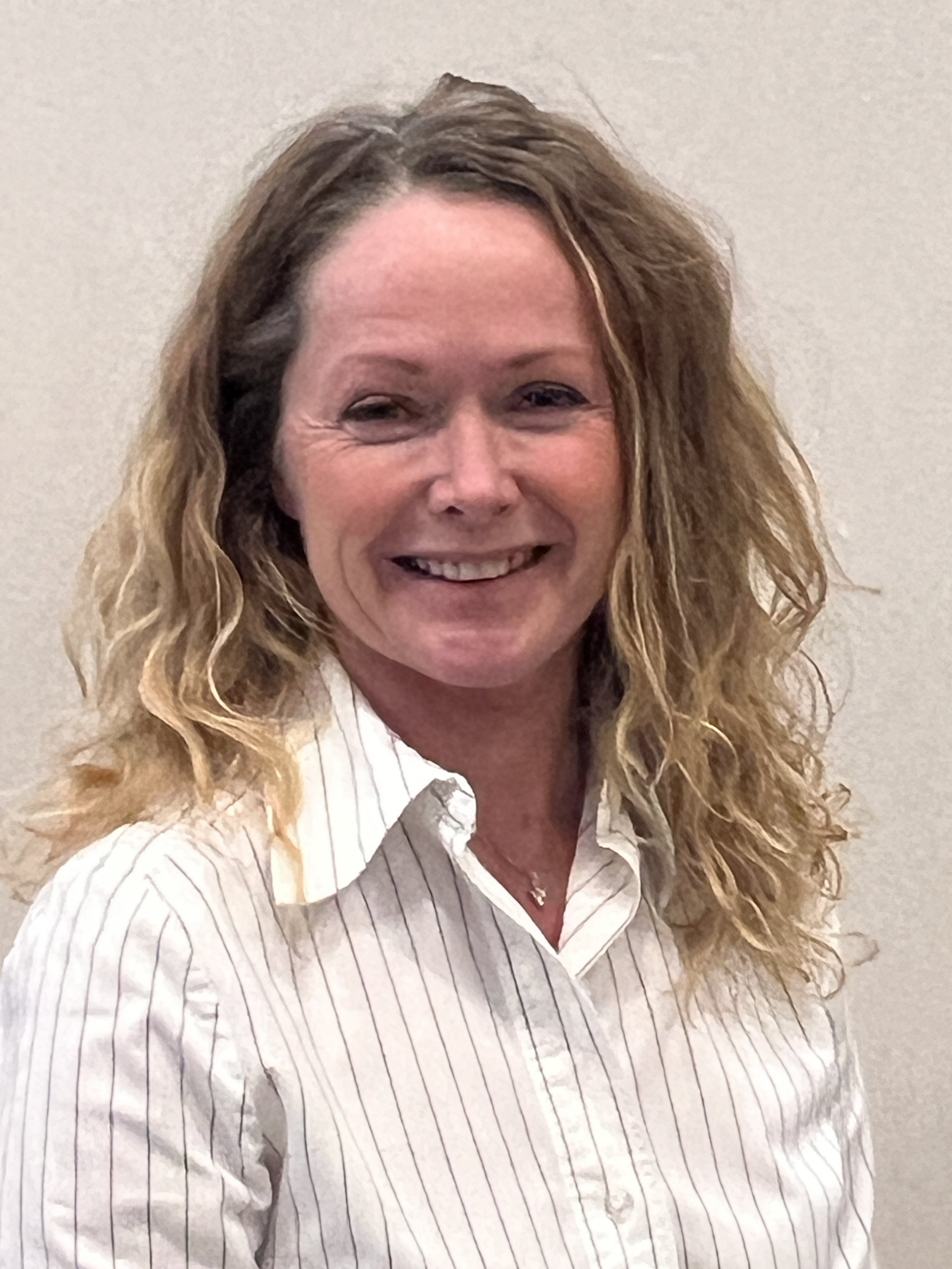 Smiling person with blond curly hair wearing a white striped shirt.