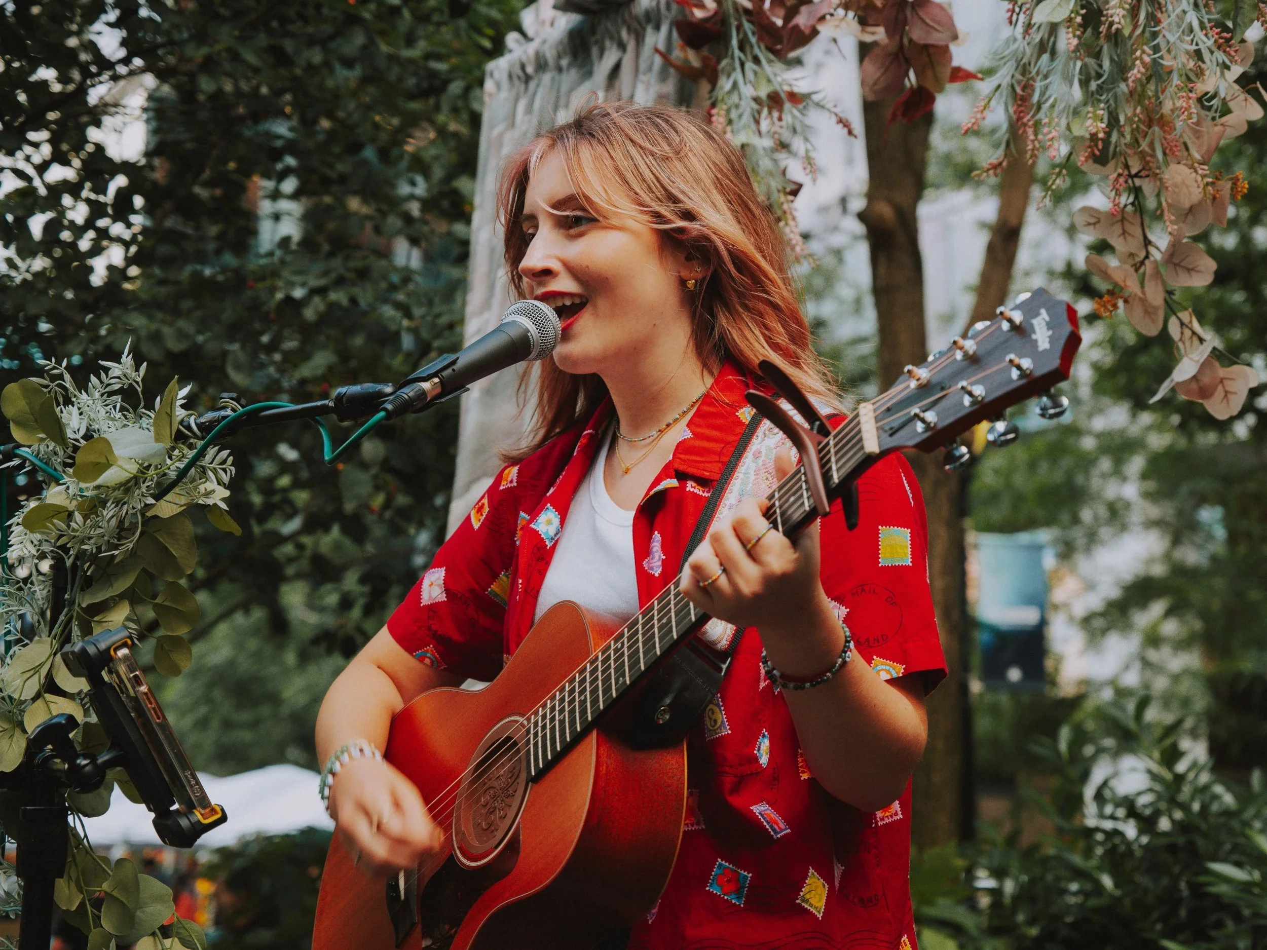 A singer-songwriter performing outdoors with an acoustic guitar — LIPAF Closing Reception solo musician open call.
