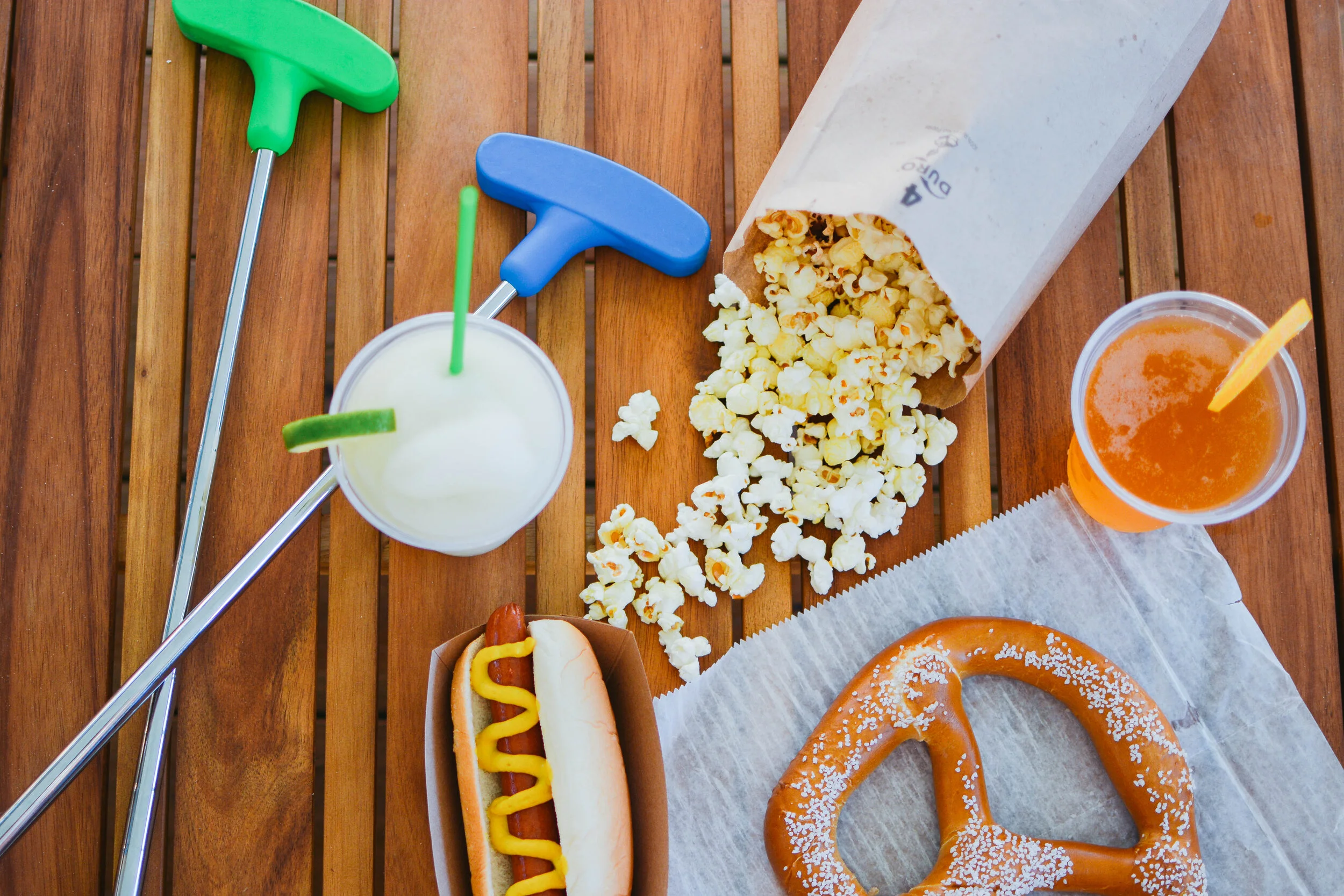 Above table view of popcorn, drink, pretzel, hotdog and golf clubs