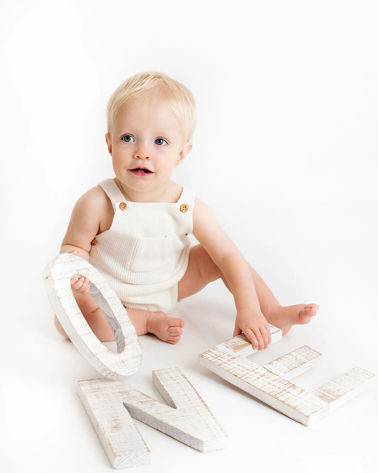 A baby sitting on the floor with white wooden letters spelling 'LOVE'.