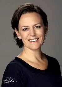 Portrait of a woman with short brown hair wearing a black top, smiling at the camera against a gray background.