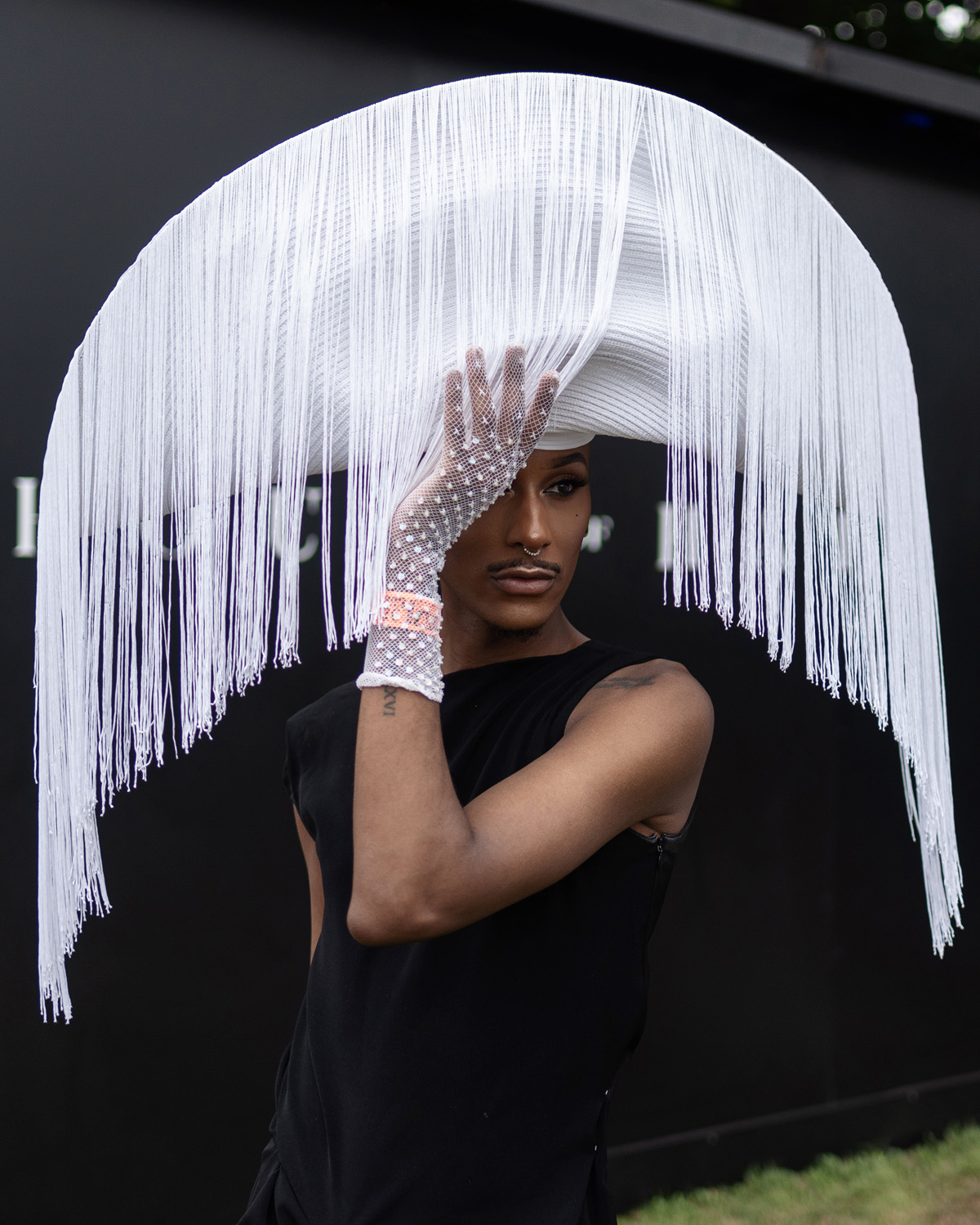 Person wearing an avant-garde hat with white fringes and mesh gloves.