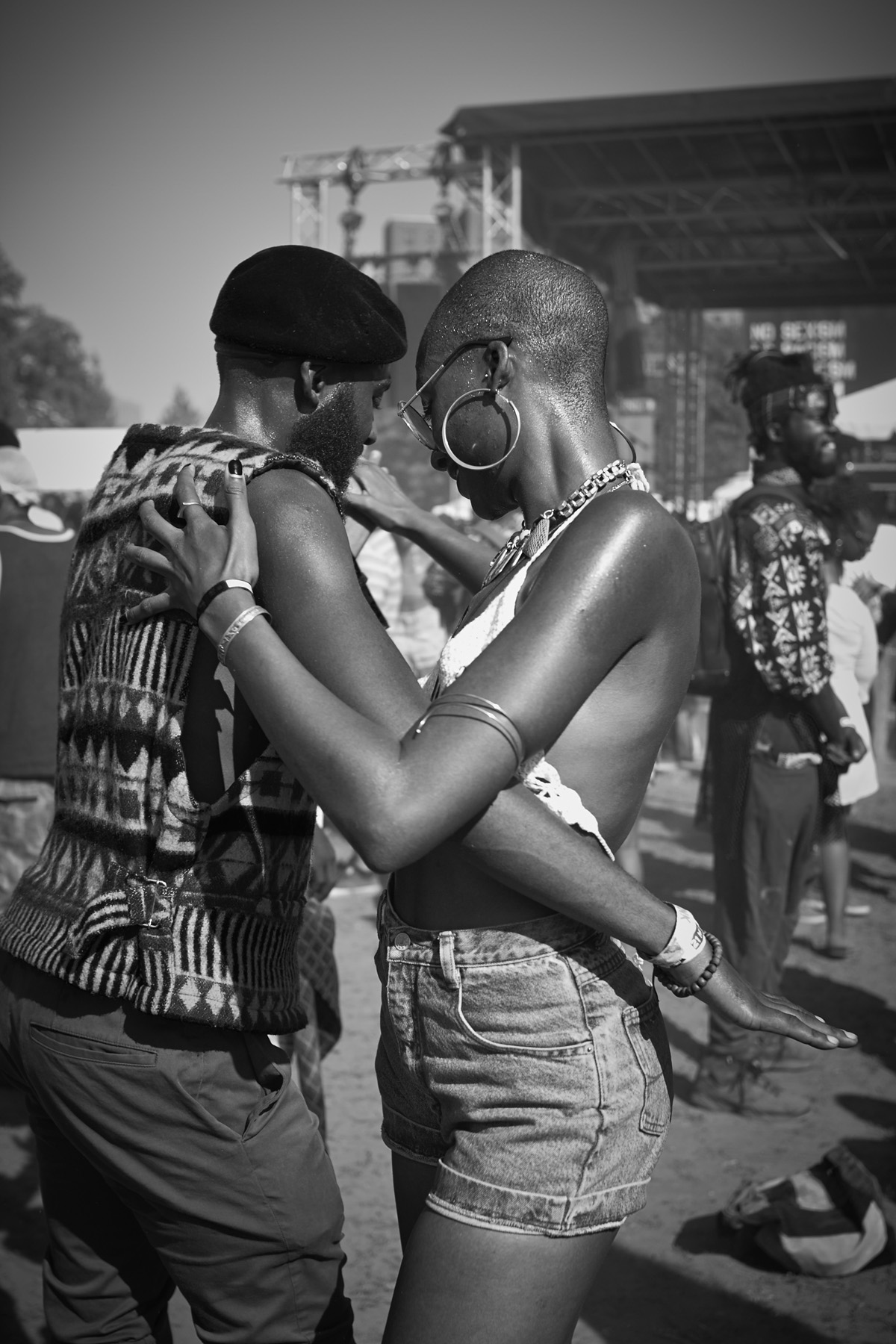 Two people dancing closely at an outdoor festival. Black and white photo, woman in denim shorts and large hoop earrings.