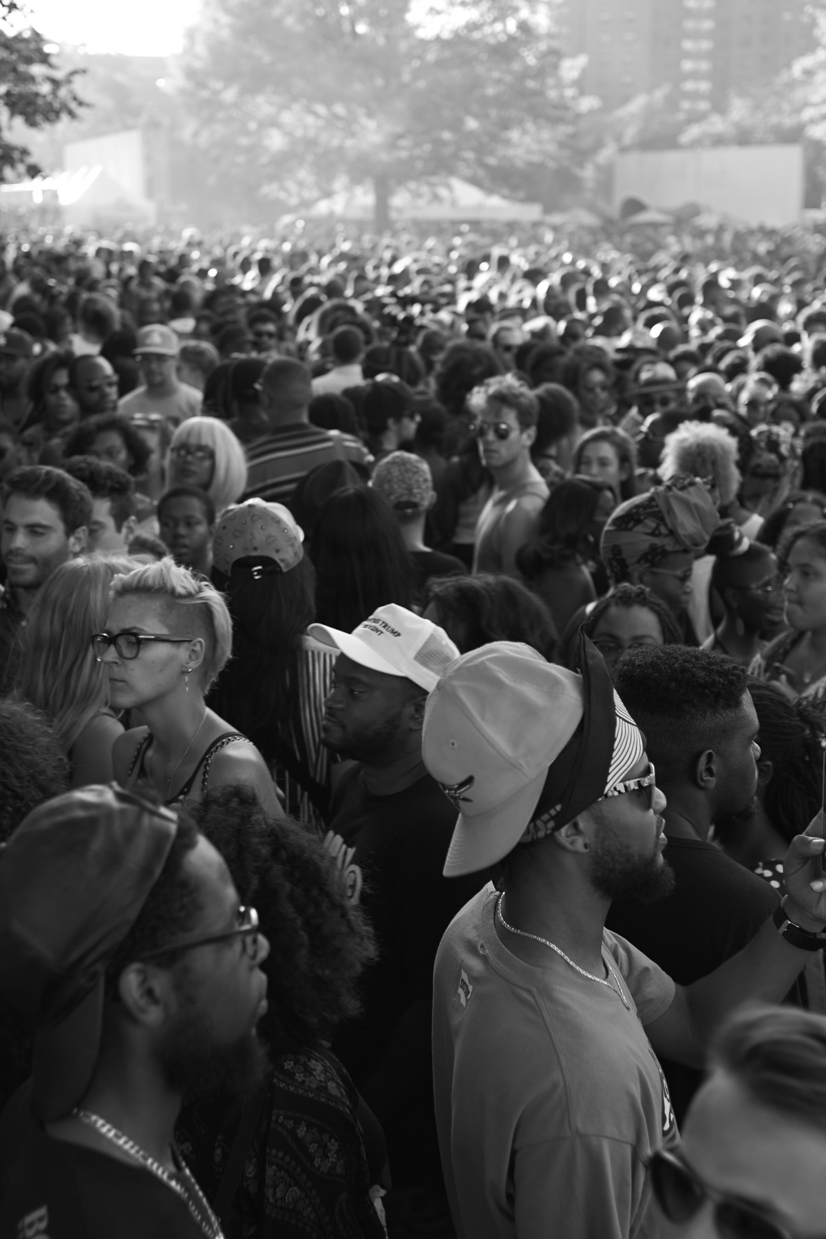 Black and white image of a large crowd at an outdoor event, people wearing various hats, sunglasses, and hairstyles.
