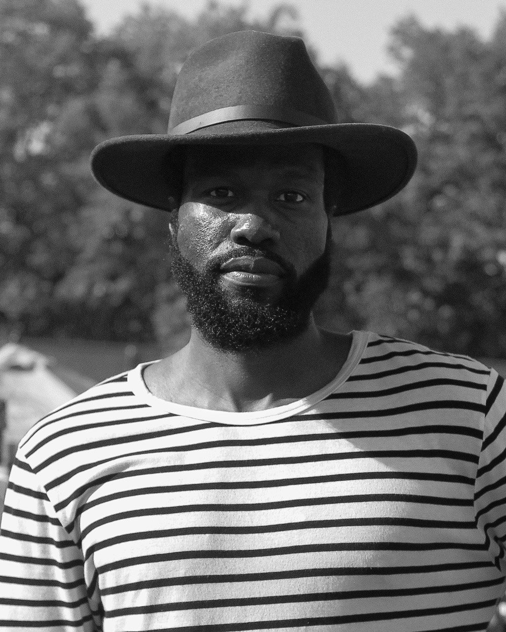 Man wearing a striped shirt and hat outdoors in black and white photo.