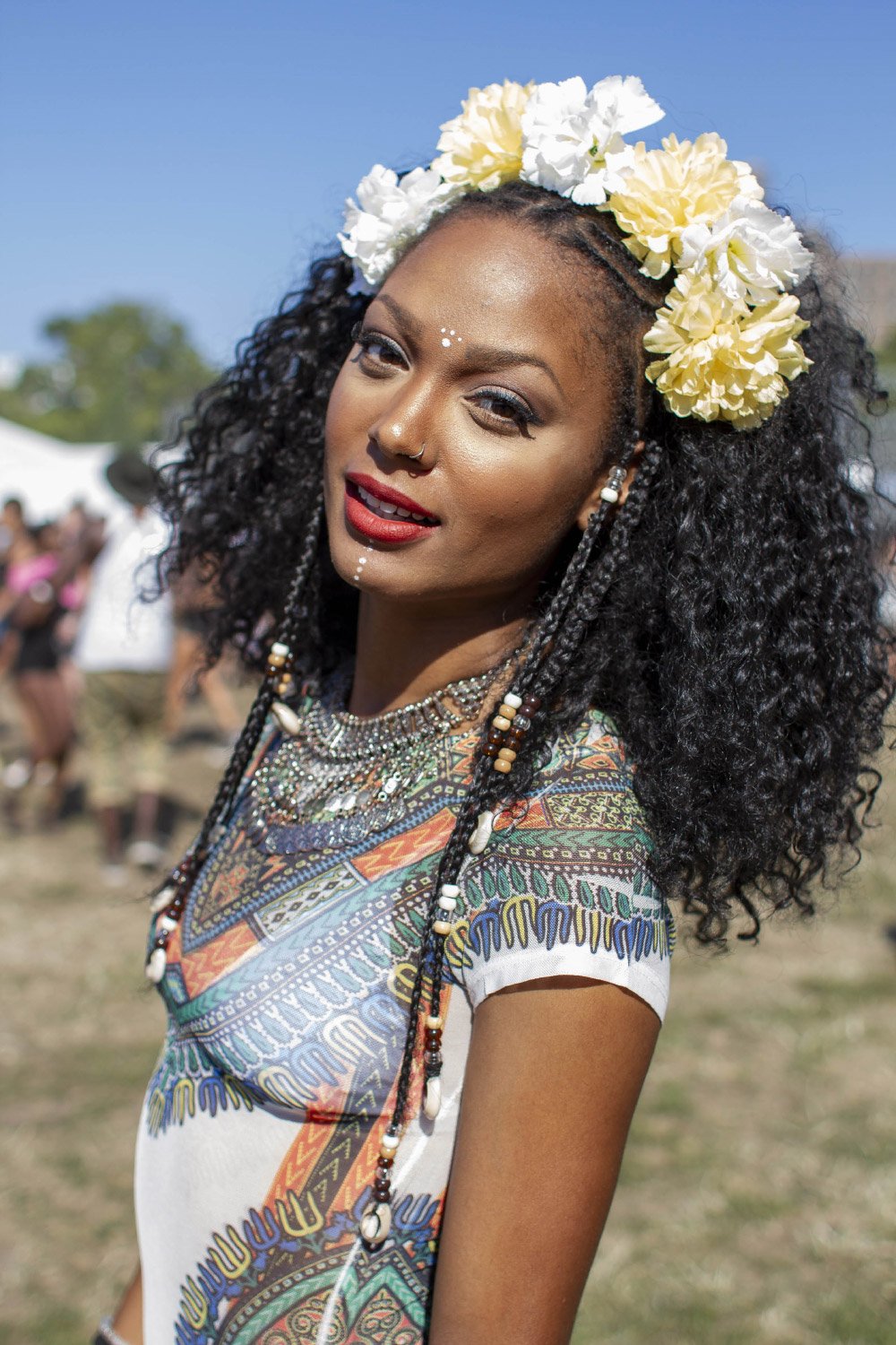Woman in colorful patterned dress with flower crown and beads, outdoor setting