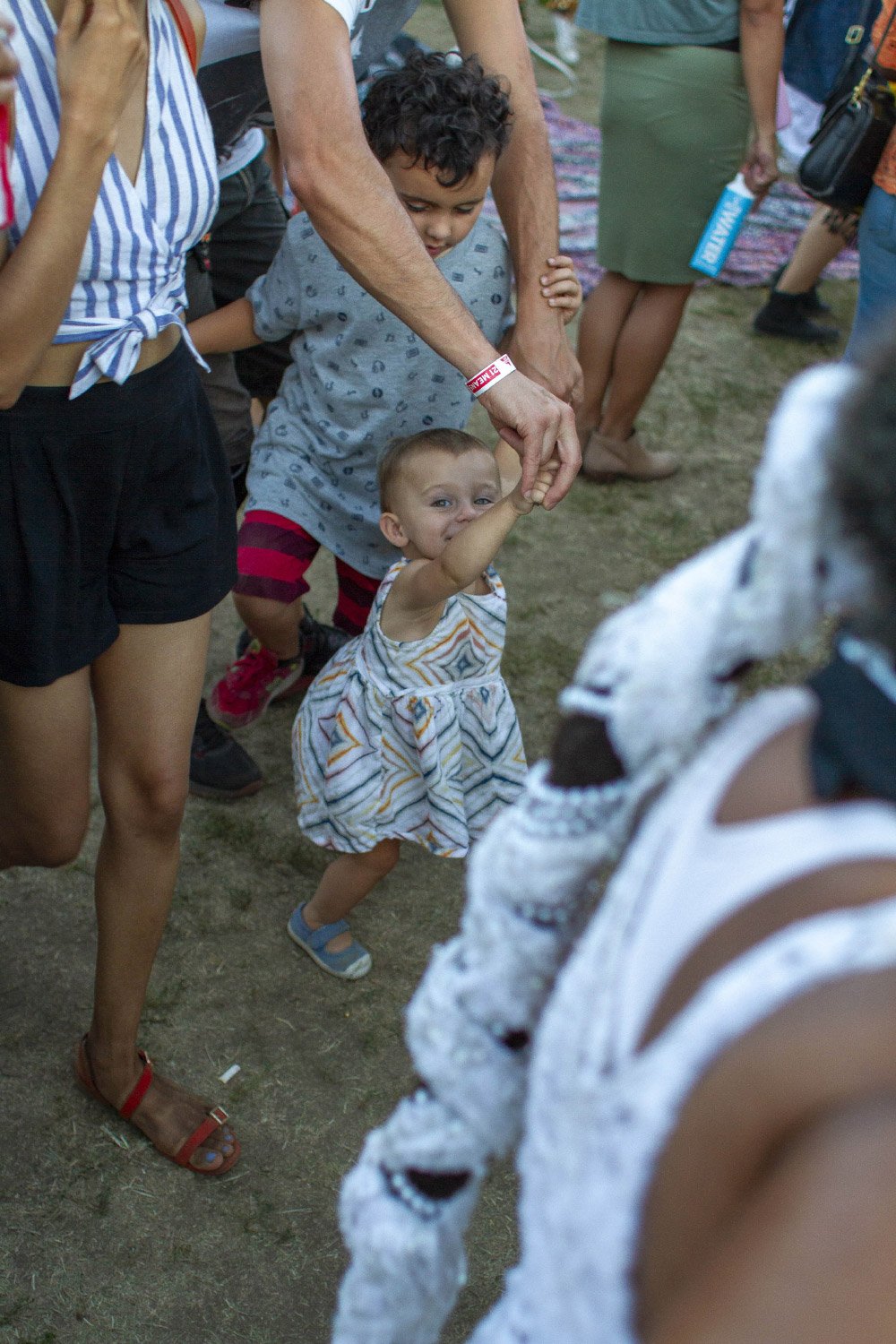 A group of children and adults walking at an outdoor event, with a child in a striped dress holding an adult's hand.