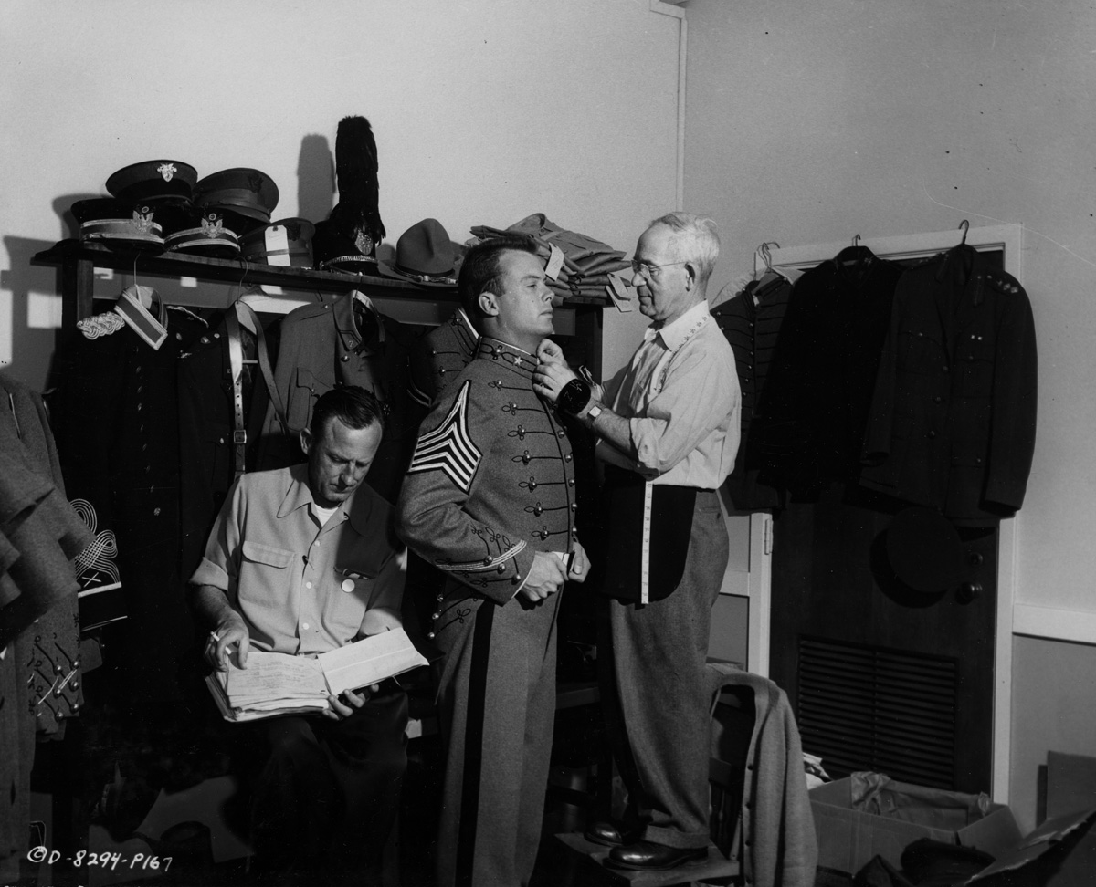  Publicity Photo, Columbia Pictures, West Point, 1954.  “While wardrobe man Forrest Butler checks his script, tailor Max Zenzipper fits Bob Francis' cadet uniform at West Point during the location filming….” 