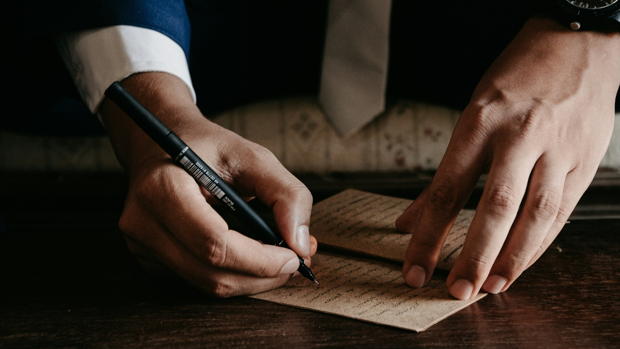 Close-up of a person writing a legal document with a black pen on a wooden desk.