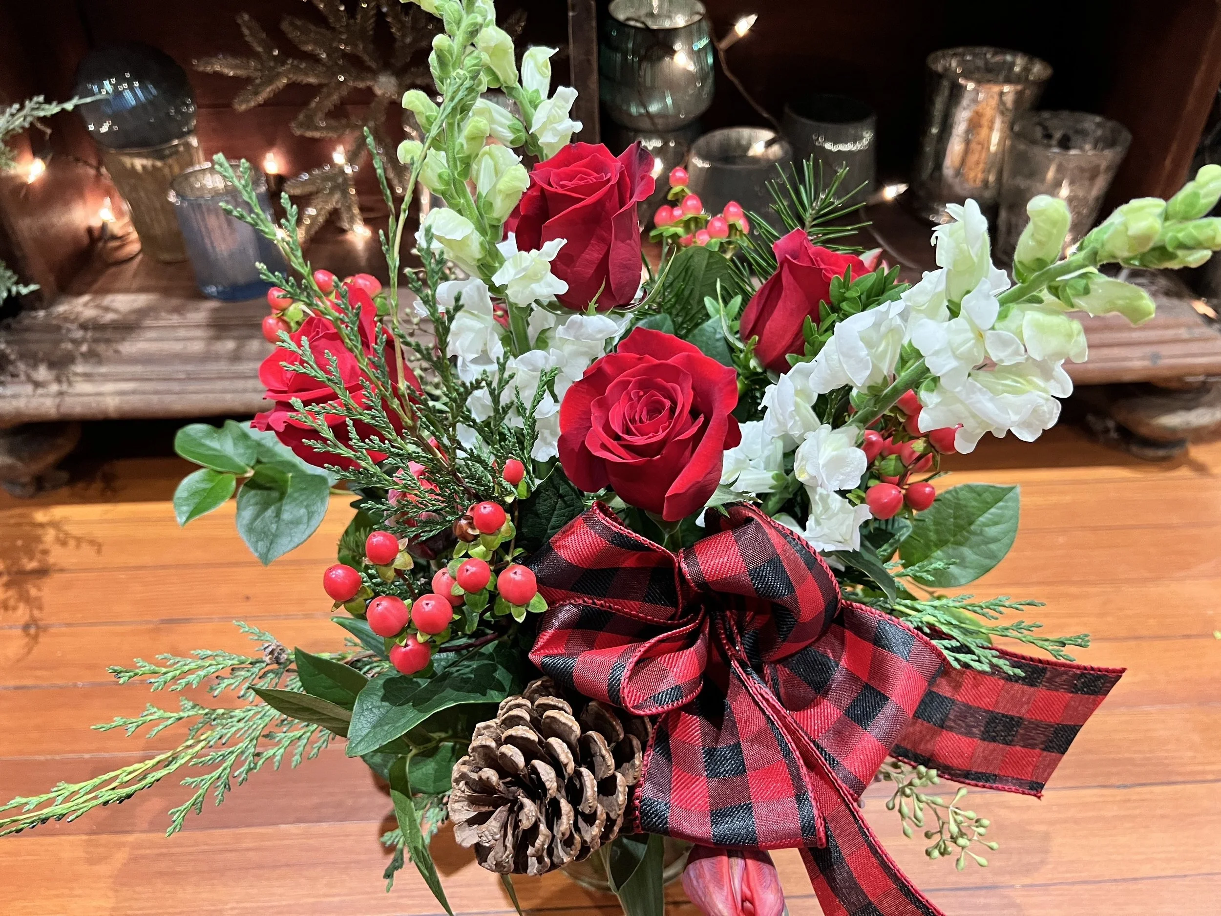 Red and white Christmas floral arrangement with snap dragon, red roses, hypericum berries, winter greens, holiday bow and pine cones.