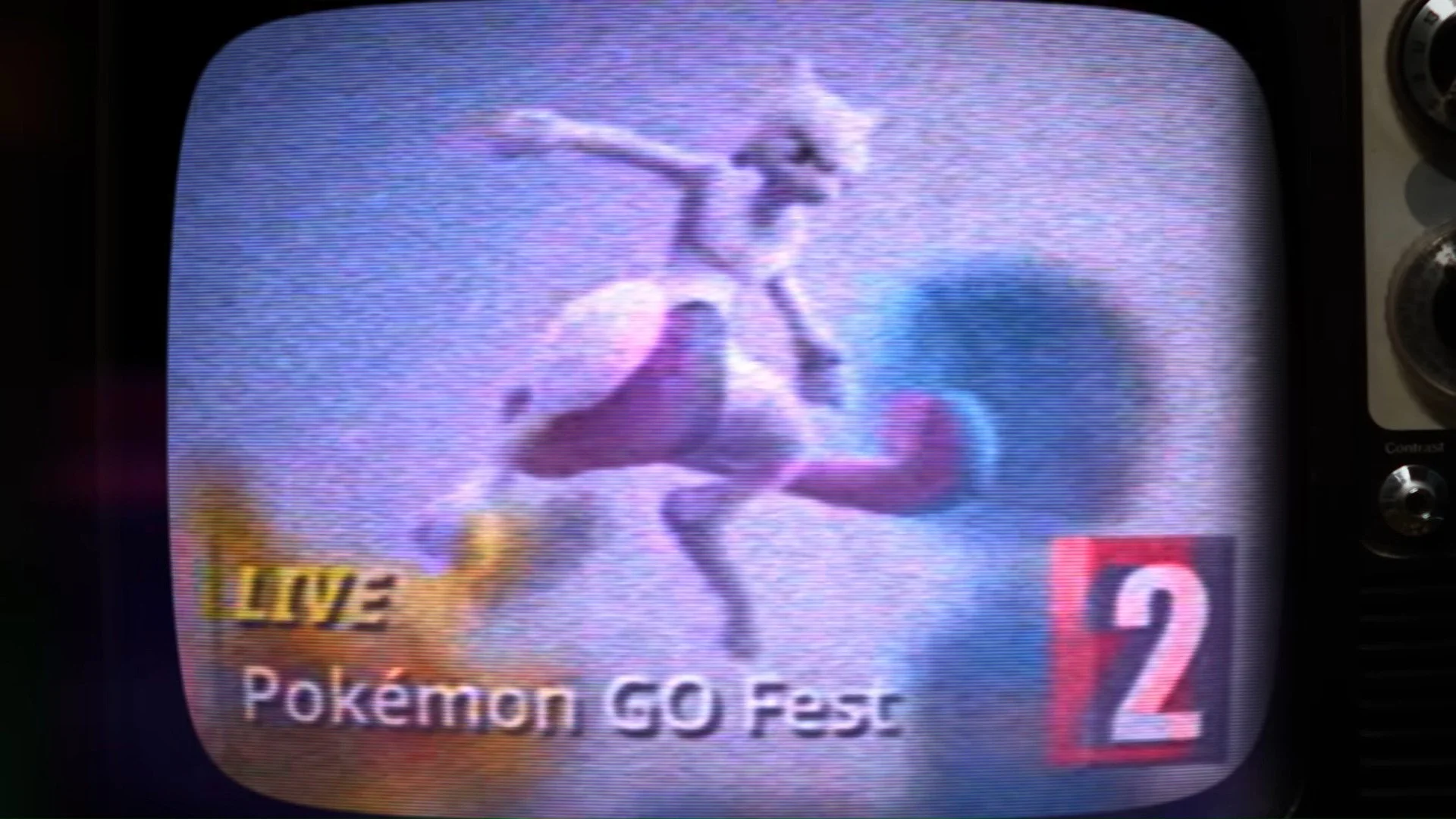 Alt text: Mewtwo poses in the sky, as seen on TV, reading “LIVE Pokemon Go Fest” on Channel 2.