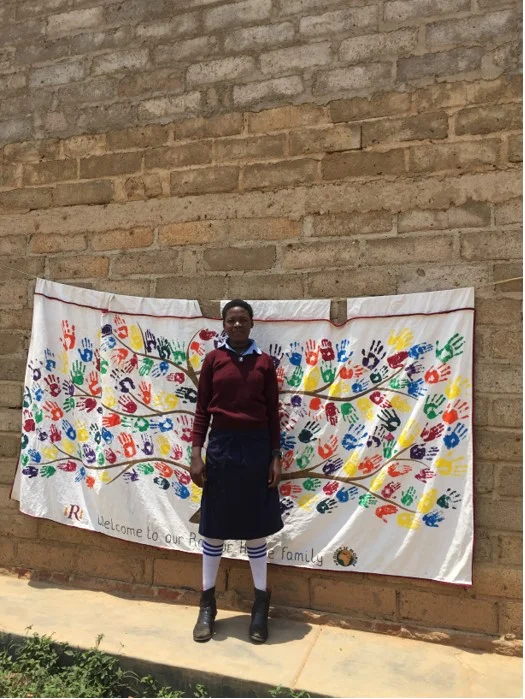 A student in school uniform beside a colourful handprint banner.