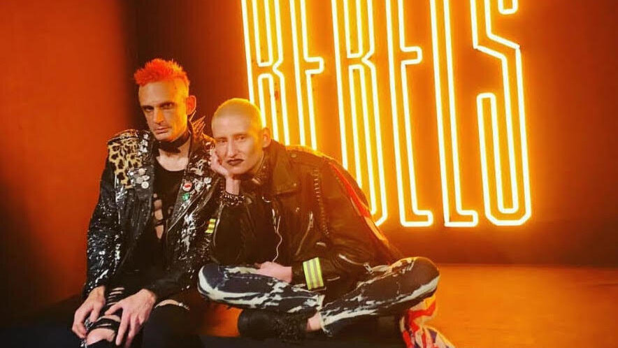  punk rockers in black leather jackets sat in front of neon rebel sign 